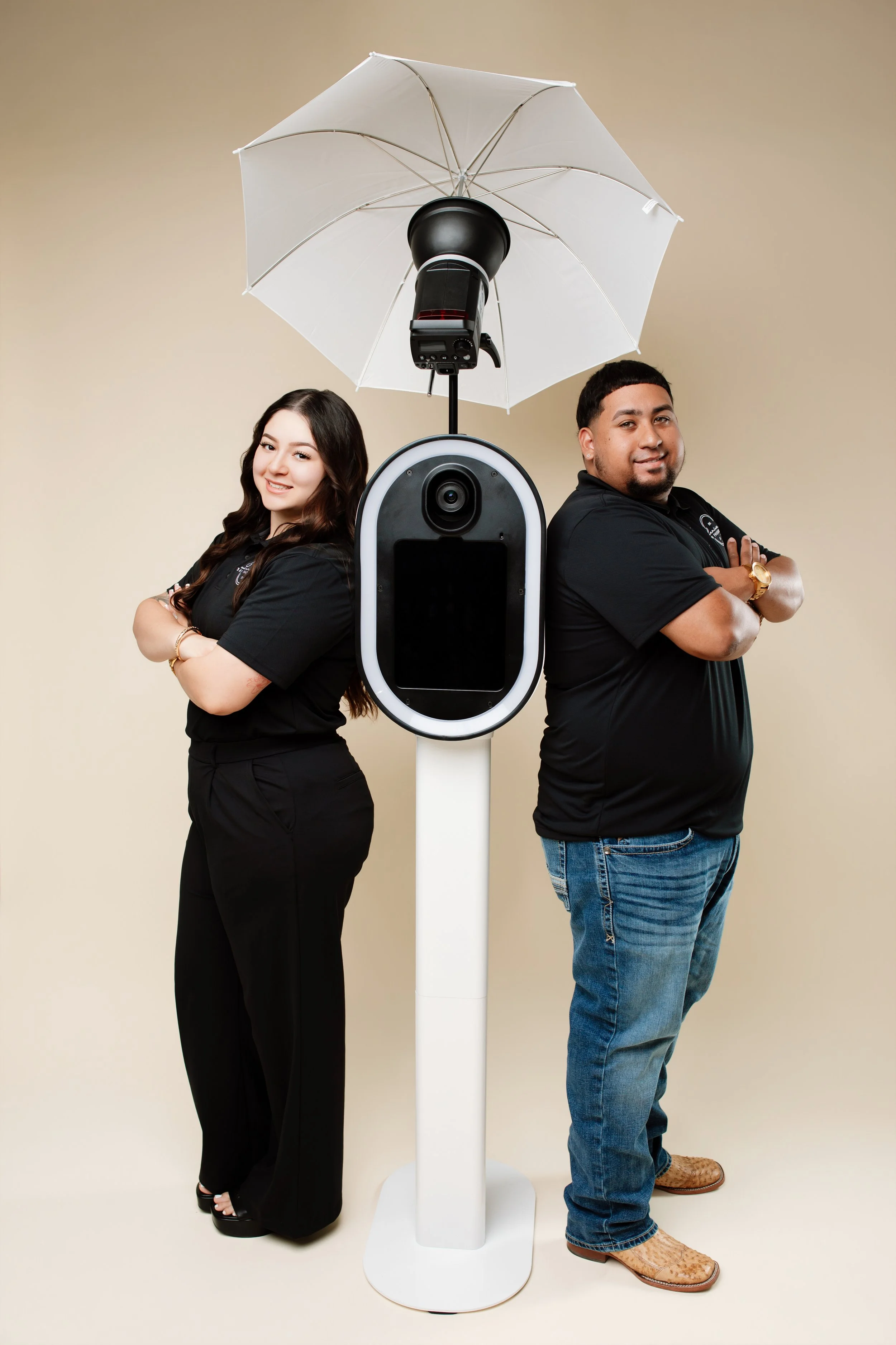 Two people standing back to back with arms crossed beside a robot with a camera on top, under a white umbrella-shaped cover.