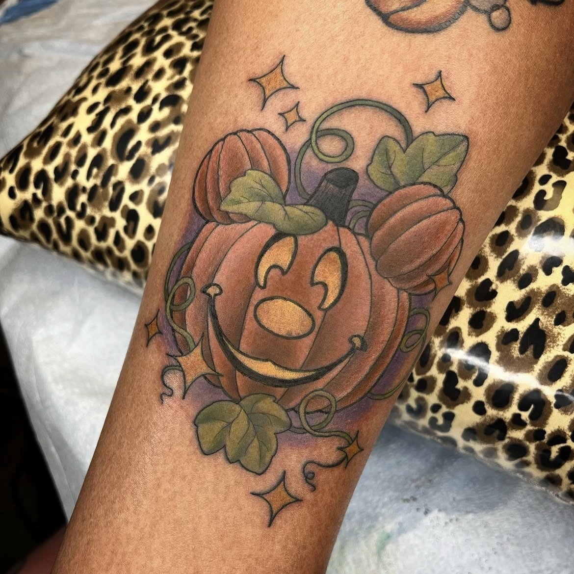 Tattoo of a jack-o'-lantern with a smiling face, surrounded by leaves and stars.