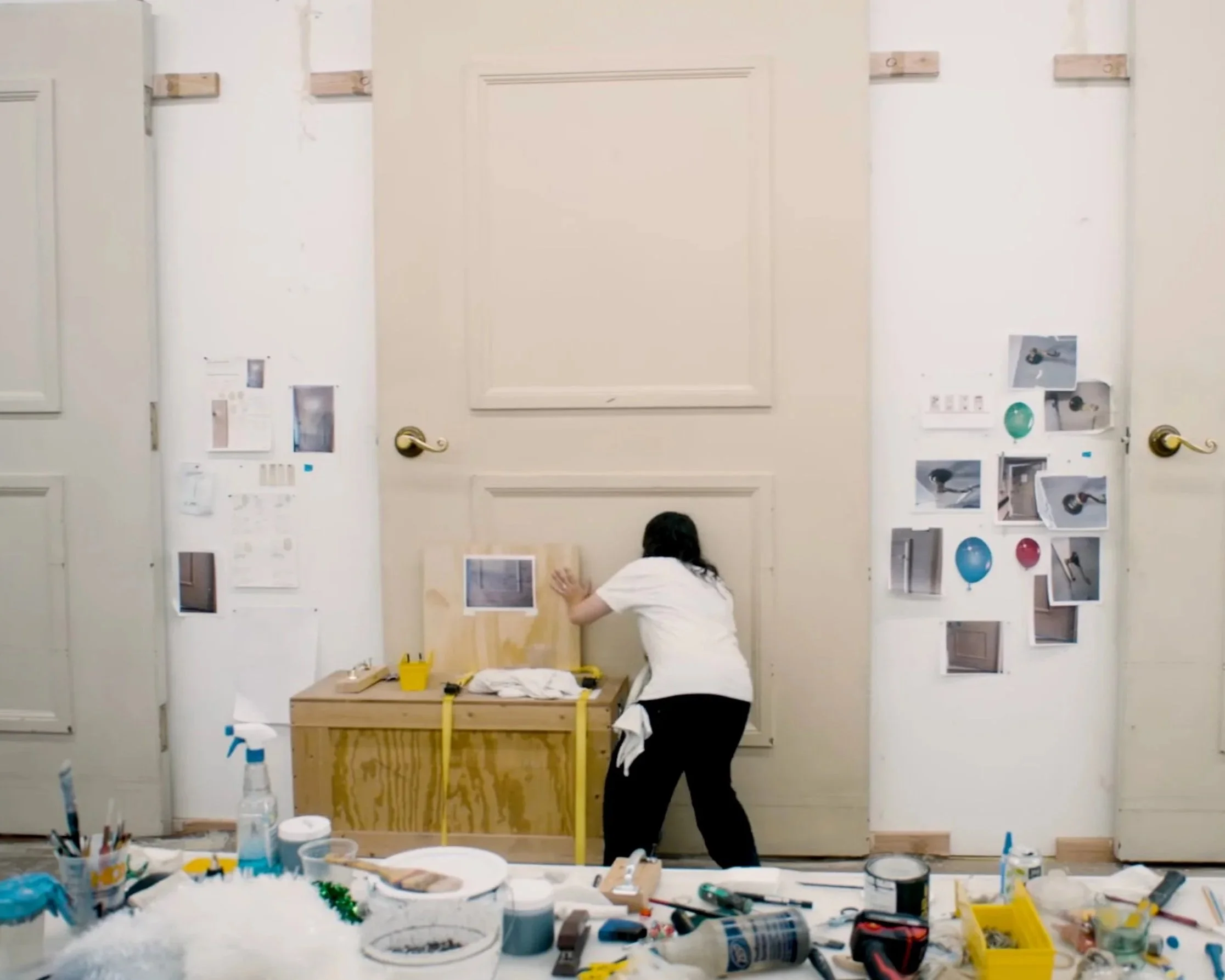 Person working on an art or craft project at a table with various supplies, some pasting pictures on a wall behind them.