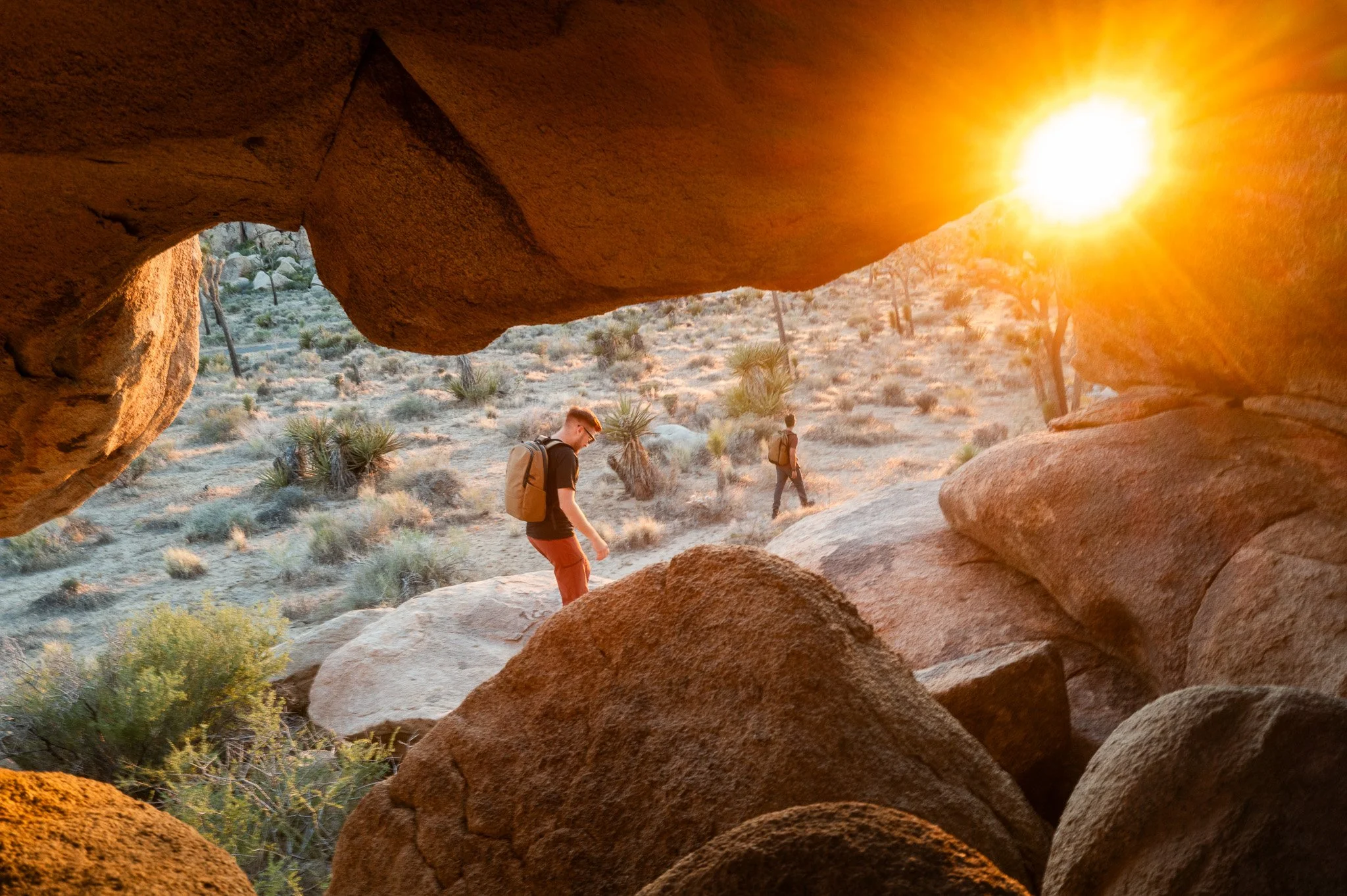 Two people hiking in a desert landscape viewed through a rock formation during sunset