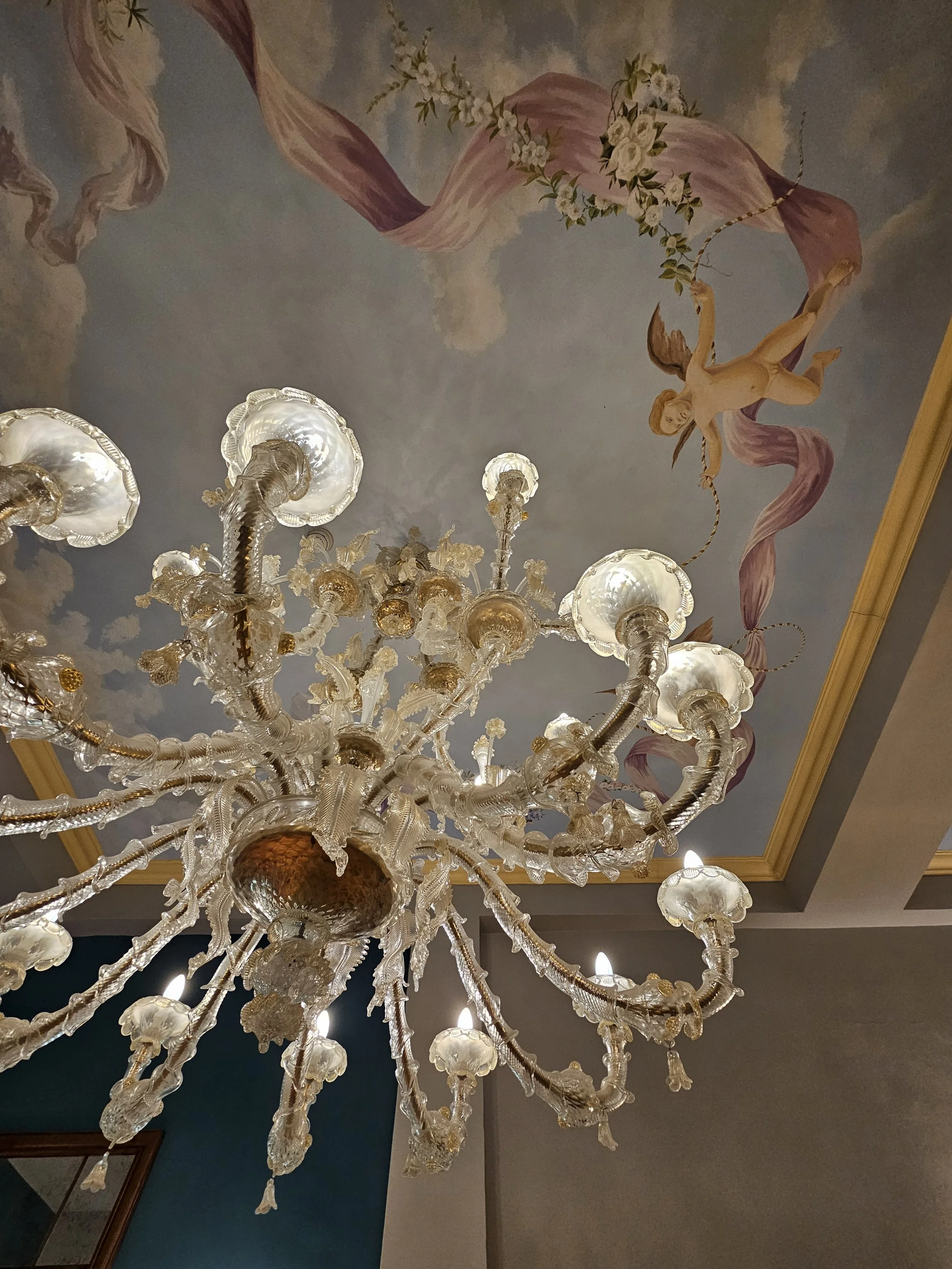 looking up at a glass chandelier with a decorated ceiling