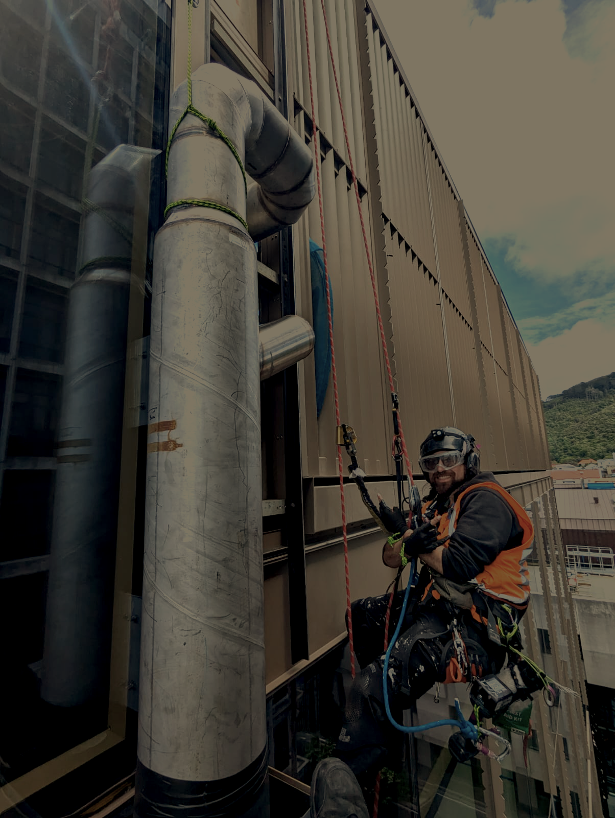 man in hi-vis hanging on climbing ropes against a skyscraper window