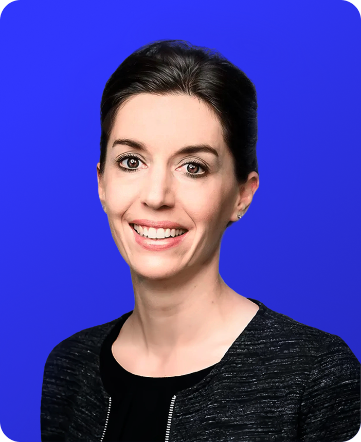 Professional woman with dark hair pulled back, smiling, wearing a black top and black jacket against a bright blue background.