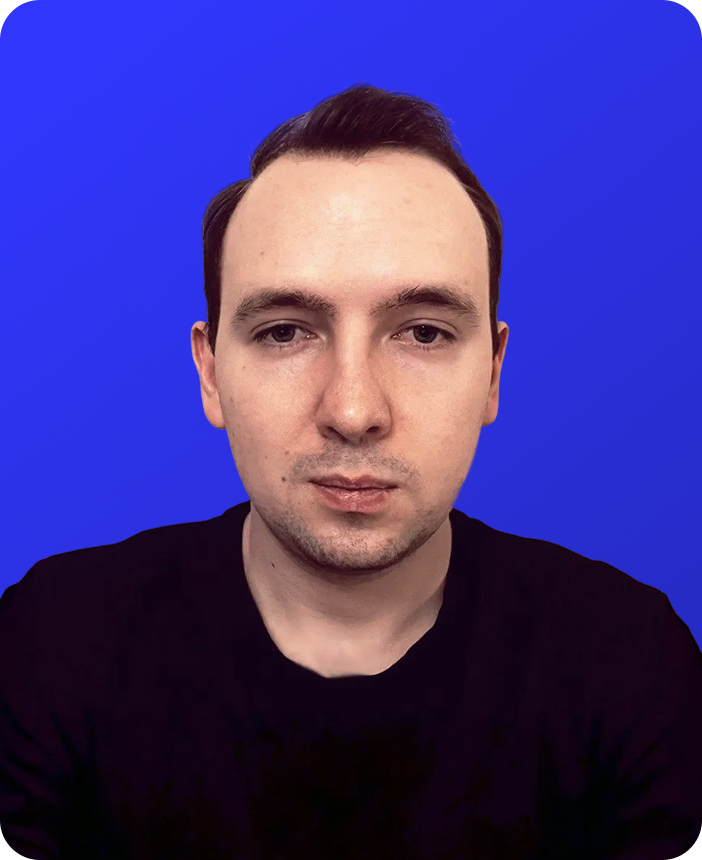 A man with short dark hair and light skin wearing a black shirt, against a solid blue background.