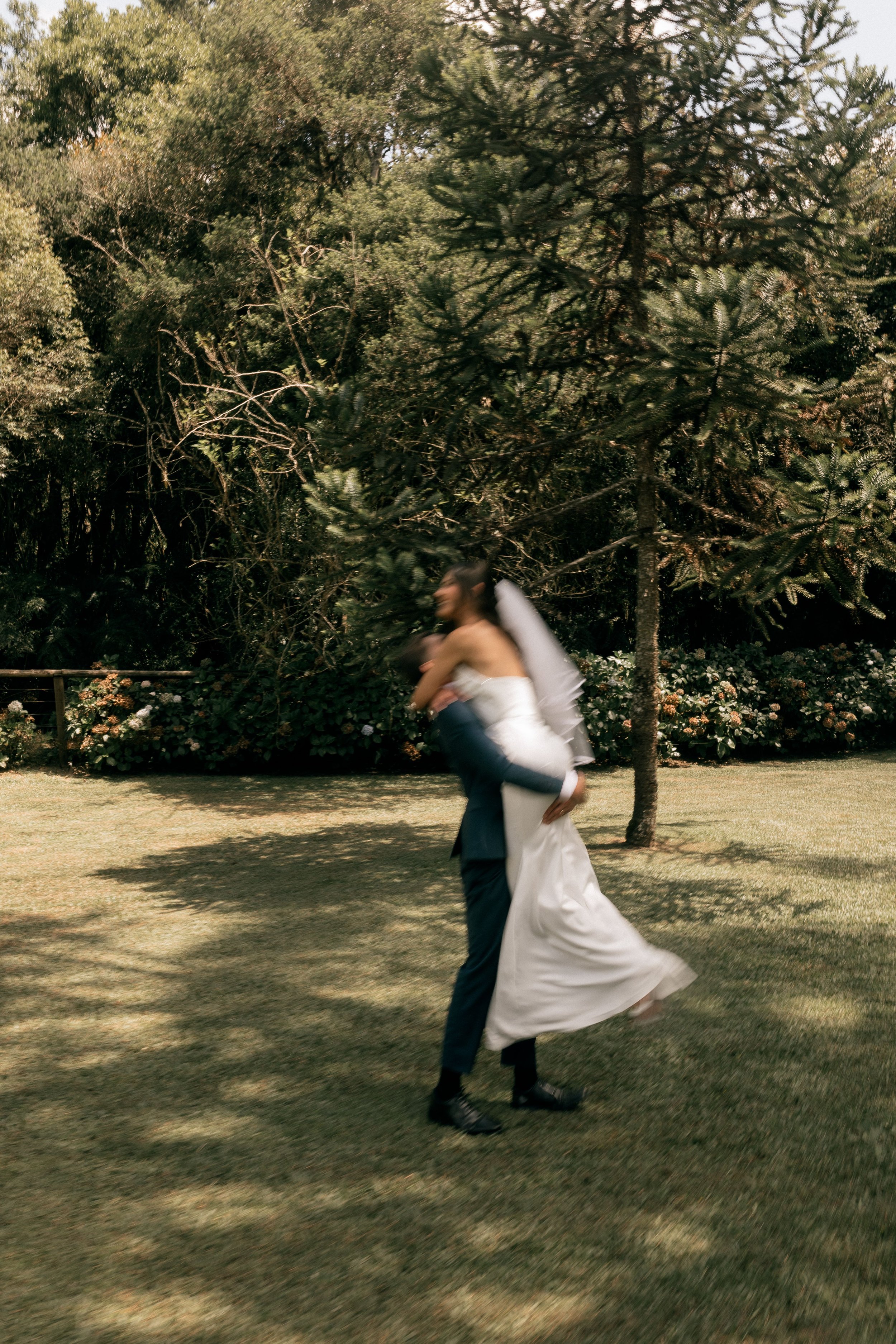 A couple dancing outdoors on a sunny day, surrounded by trees and flowers.