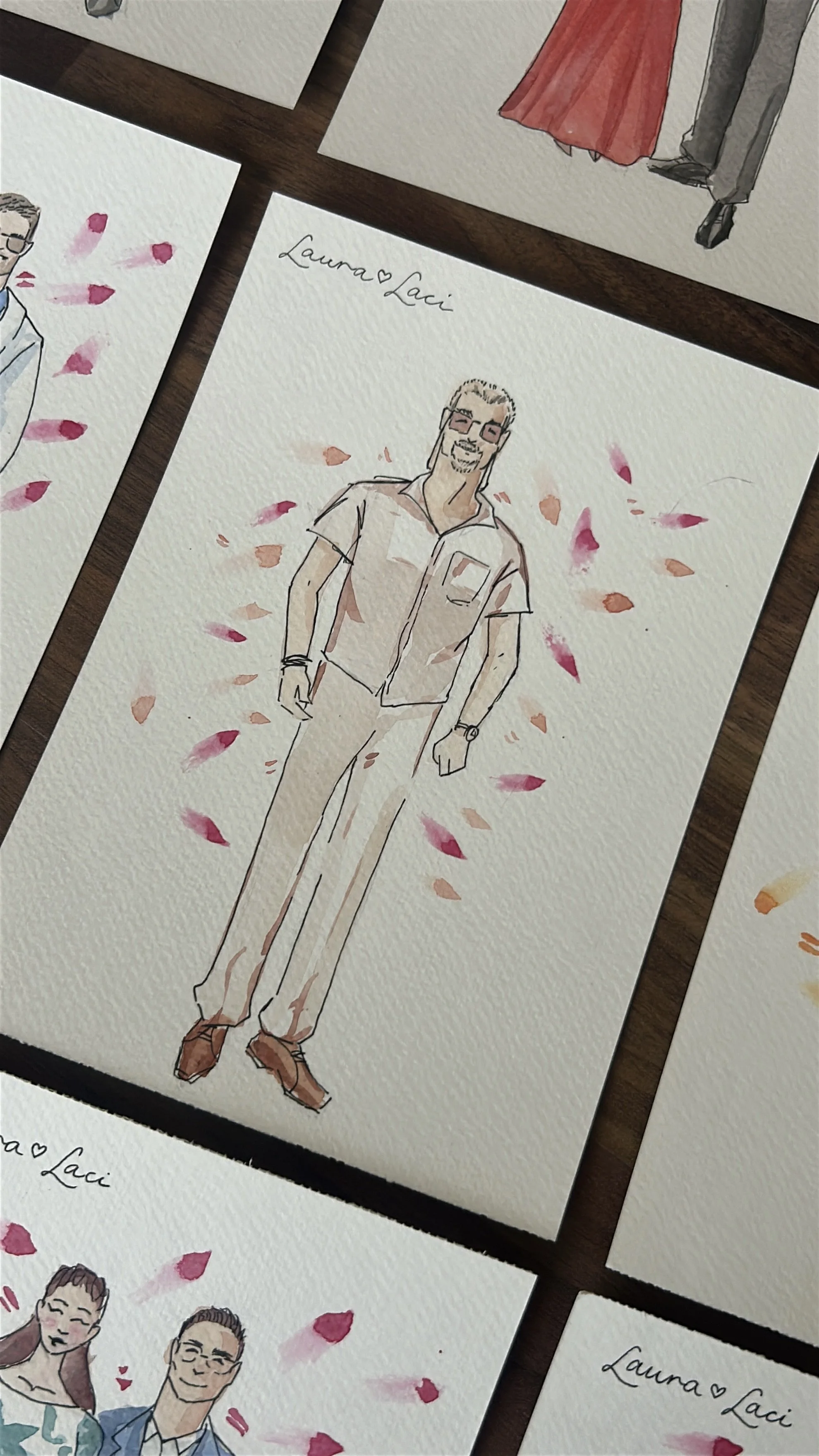 Watercolor illustration of a man with glasses and a beard, wearing a light-colored shirt and pants, standing with pink and peach flower petals around him on watercolor paper. The top left corner has a handwritten note 'Laura ♥ Laci'.