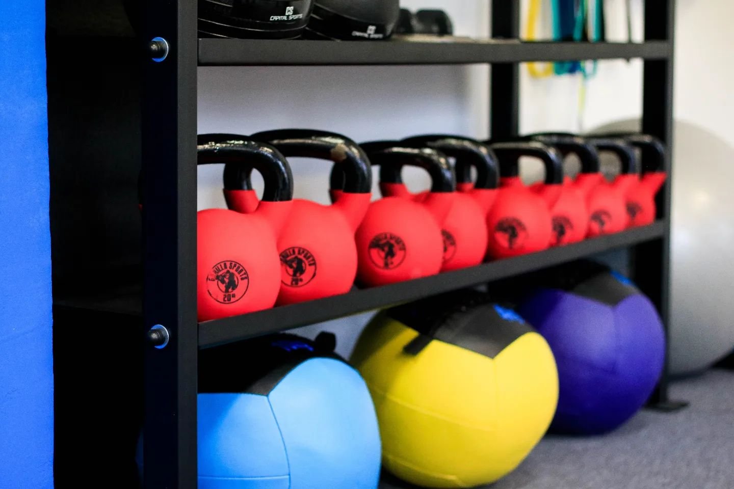 Gym equipment rack with red kettlebells and colorful medicine balls