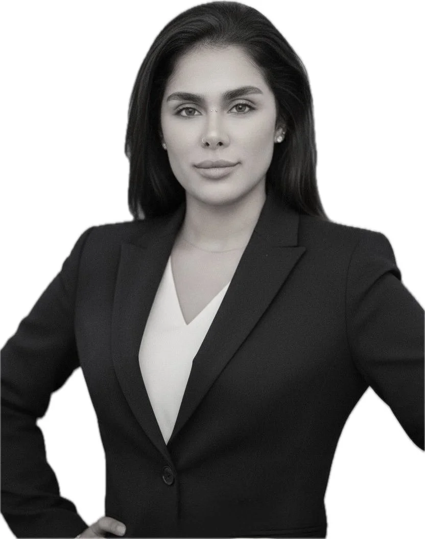 Schwarz-weiße Porträtaufnahme einer selbstbewussten jungen Frau in formeller Kleidung mit schwarzen Haaren, einem schwarzen Blazer und einer weißen Bluse vor weißem Hintergrund.