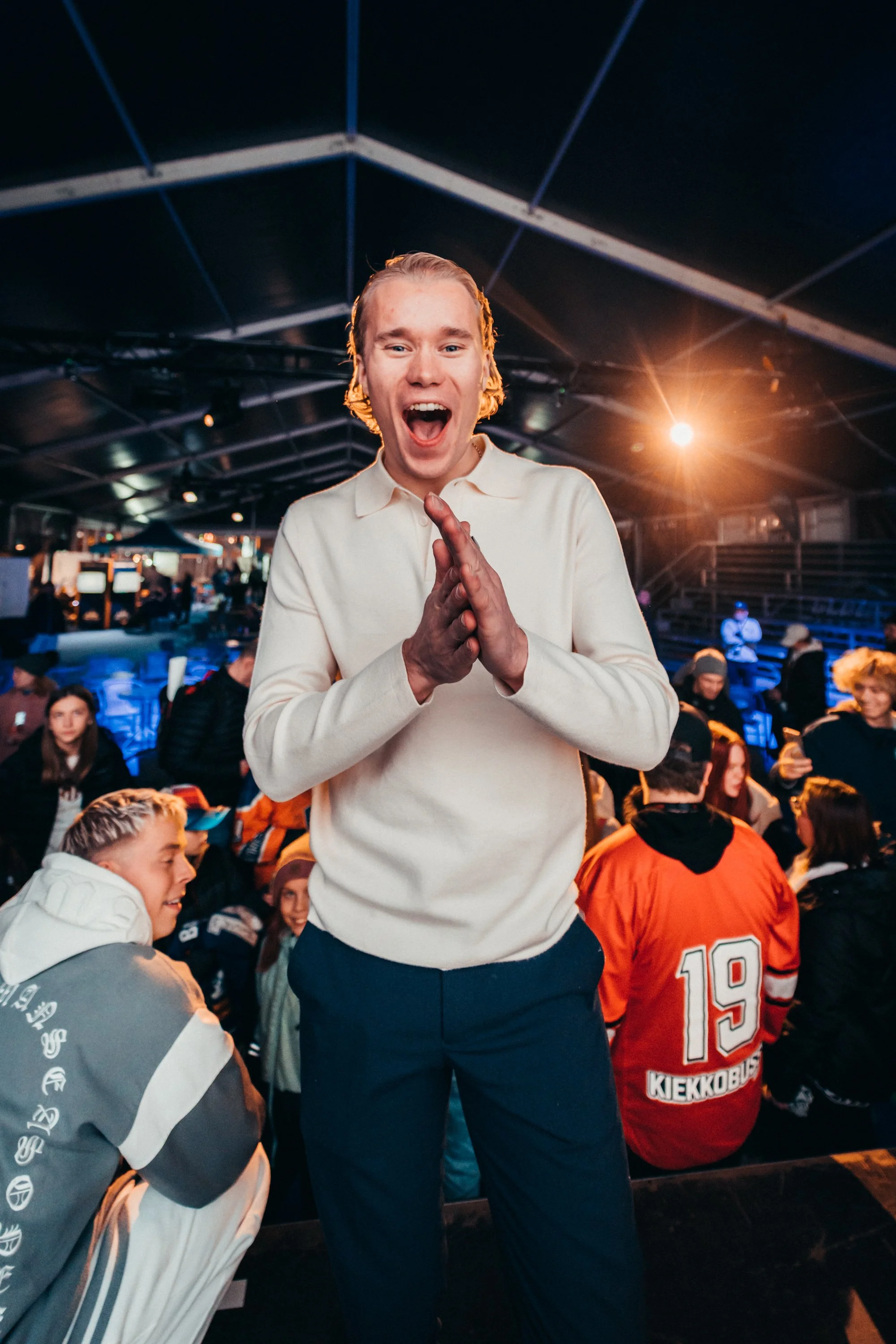 Hymyilevä nuori mies juhlatunnelmissa, taustalla muita ihmisiä.