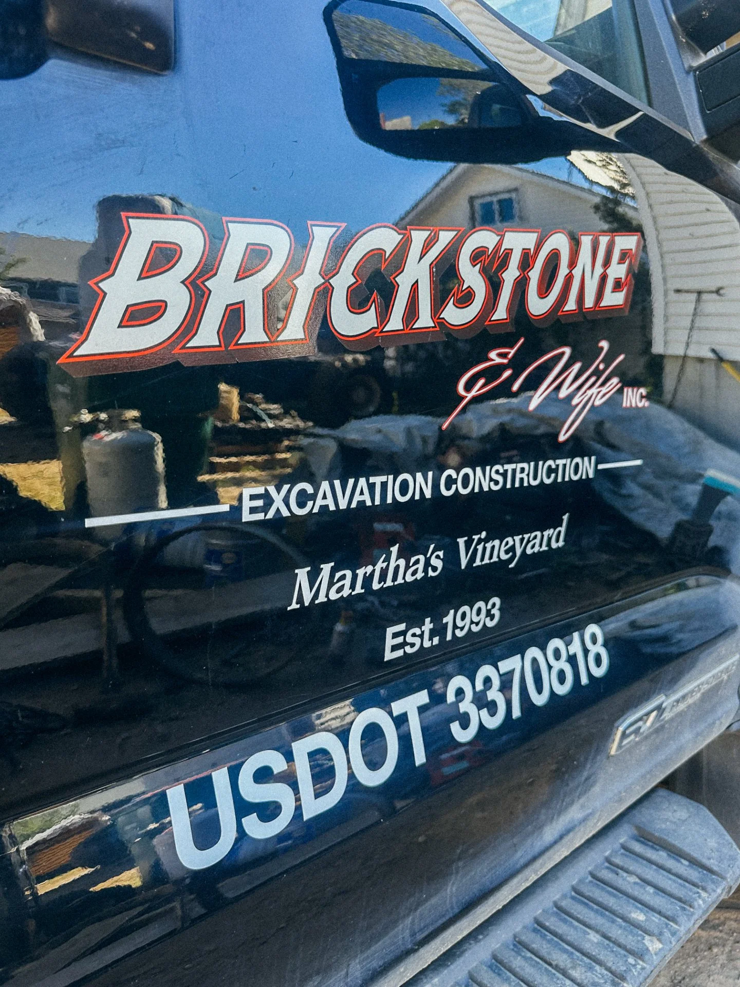 The image shows the side of a black vehicle with markings for a business named 'Brackstone & Wife Inc.' The signage indicates they offer excavation and construction services, located at Martha's Vineyard, established in 1993, with contact phone numbe