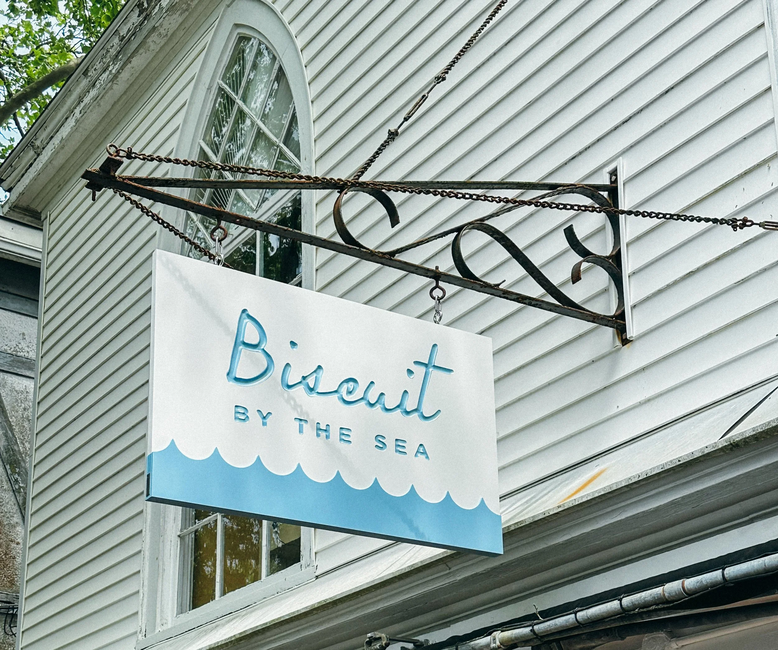 Rusty outdoor sign with chains hanging in front, attached to a building with white siding, featuring a window and a sign with blue and white colors.