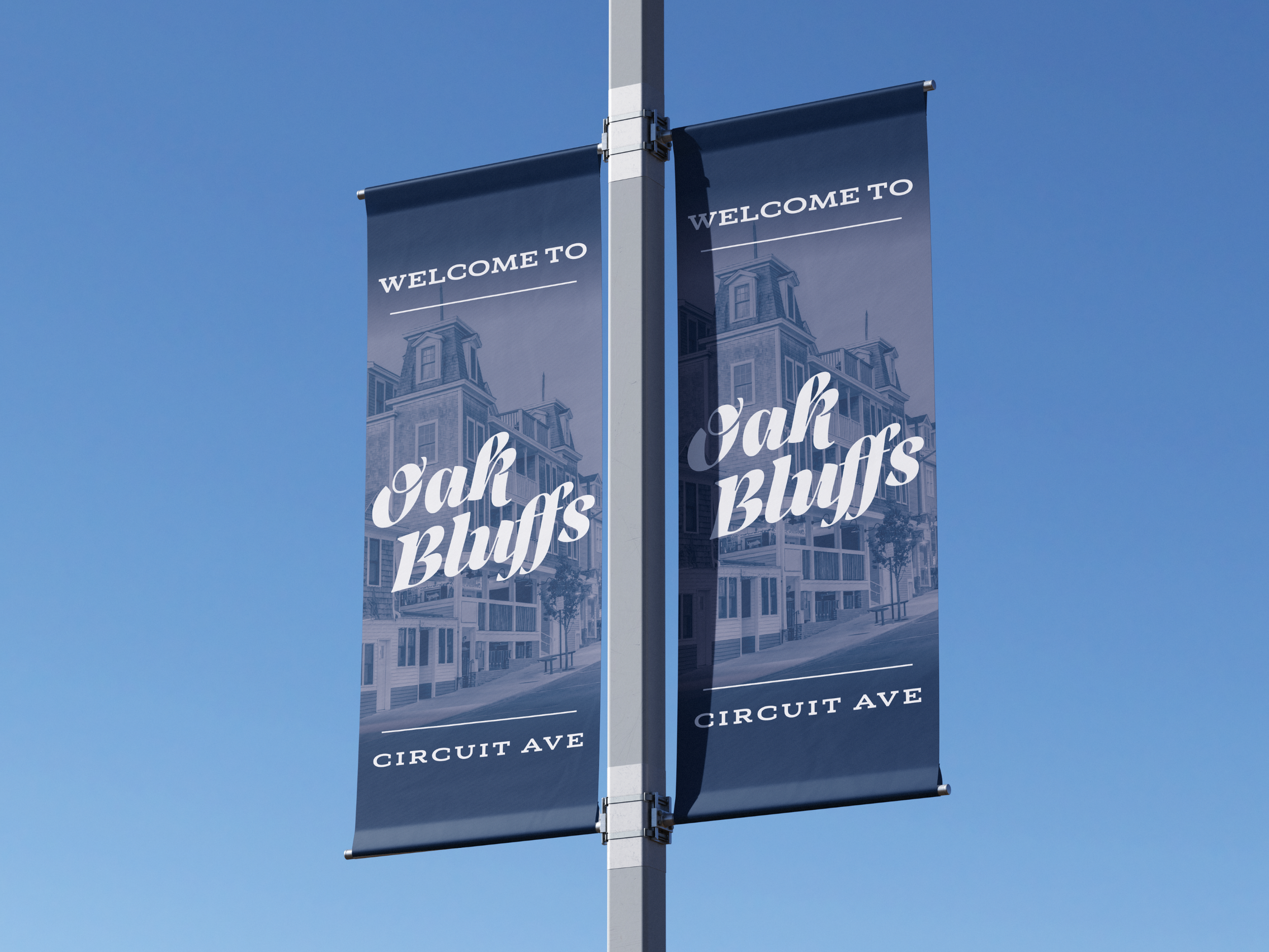 Two vertical banners on a pole welcoming visitors to Oak Bluffs on Circuit Avenue, with an illustration of a Victorian-style house against a blue sky.