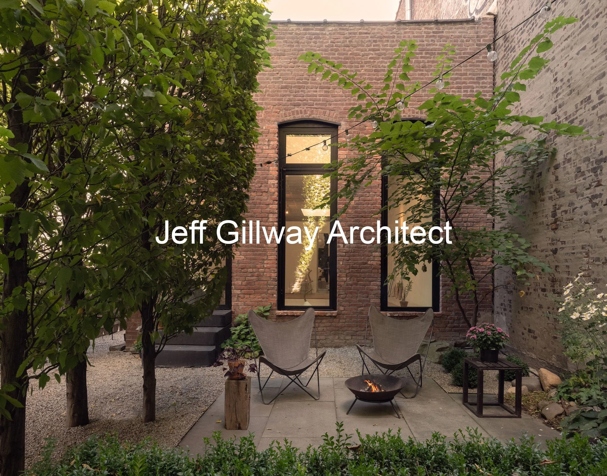 An outdoor courtyard with brick walls, trees, a patio area with two chairs, a fire pit, and a small table with flowers, with the text 'Jeff Gillway Architect' overlaid.