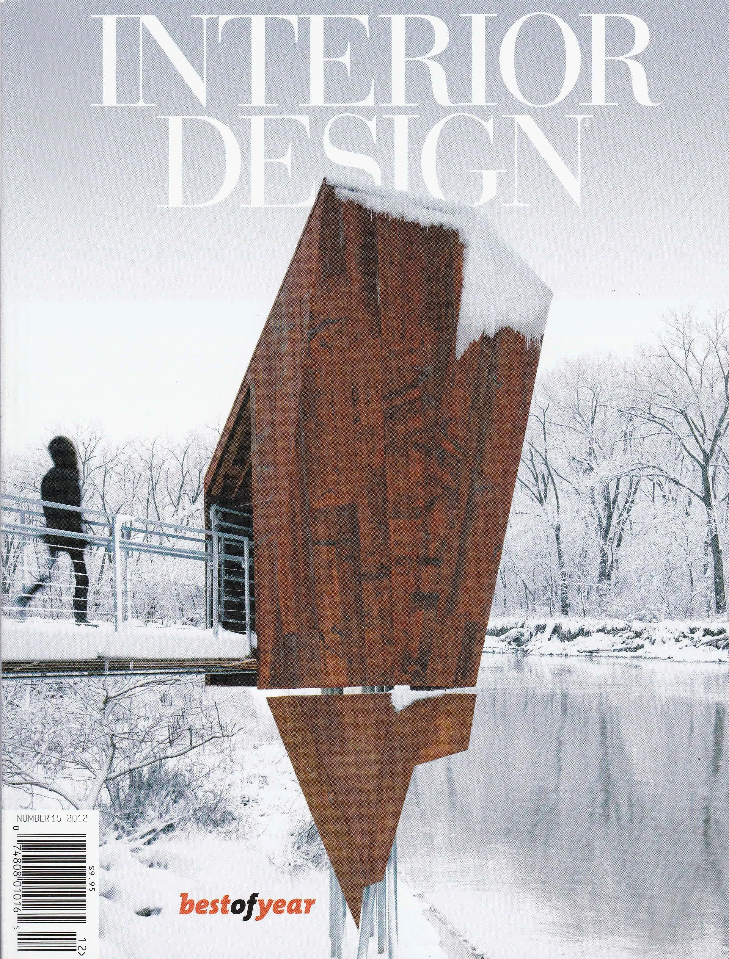 Cover of Interior Design magazine, winter scene with a modern wooden architecture structure reflecting in a river, snow-covered trees in background, person walking on the bridge.