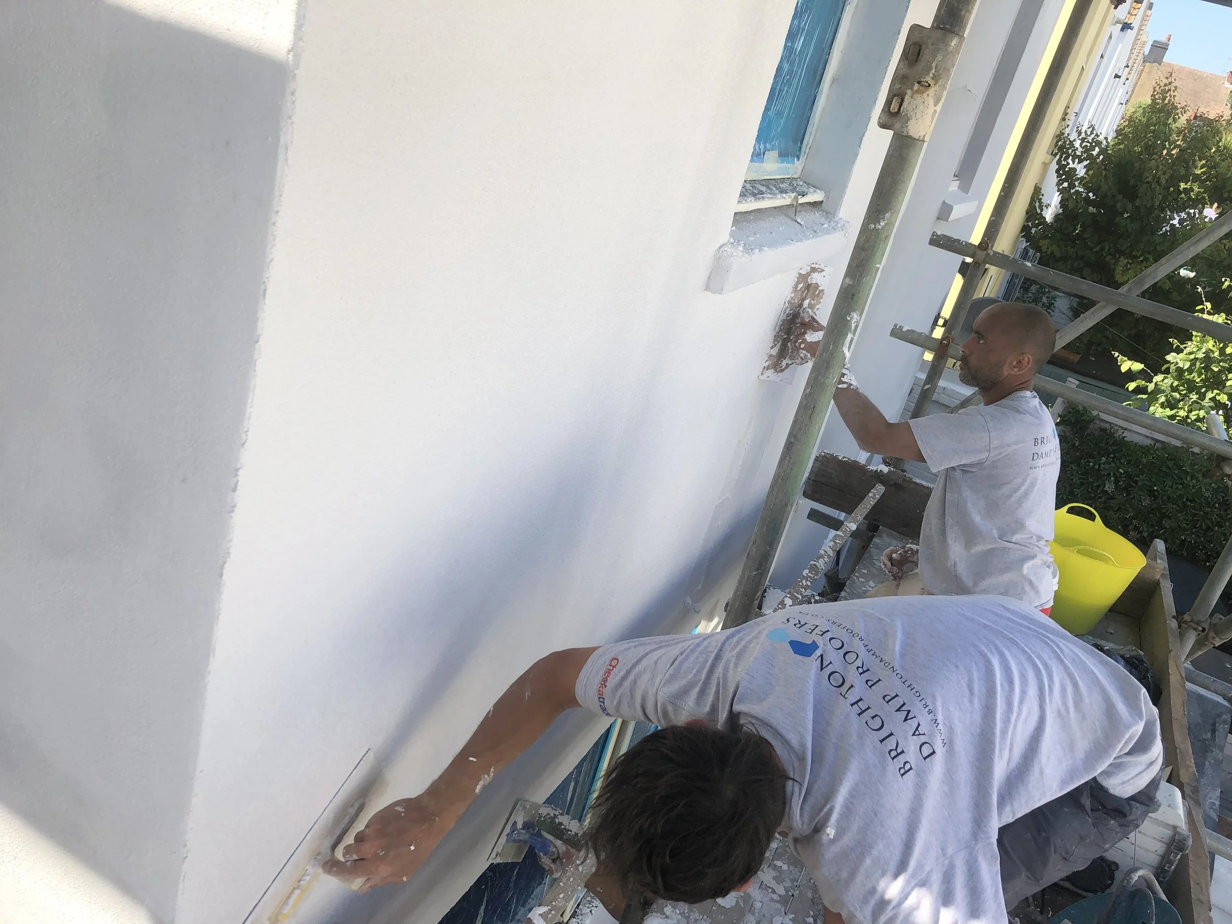 Two workers rendering an exterior wall to prevent damp.