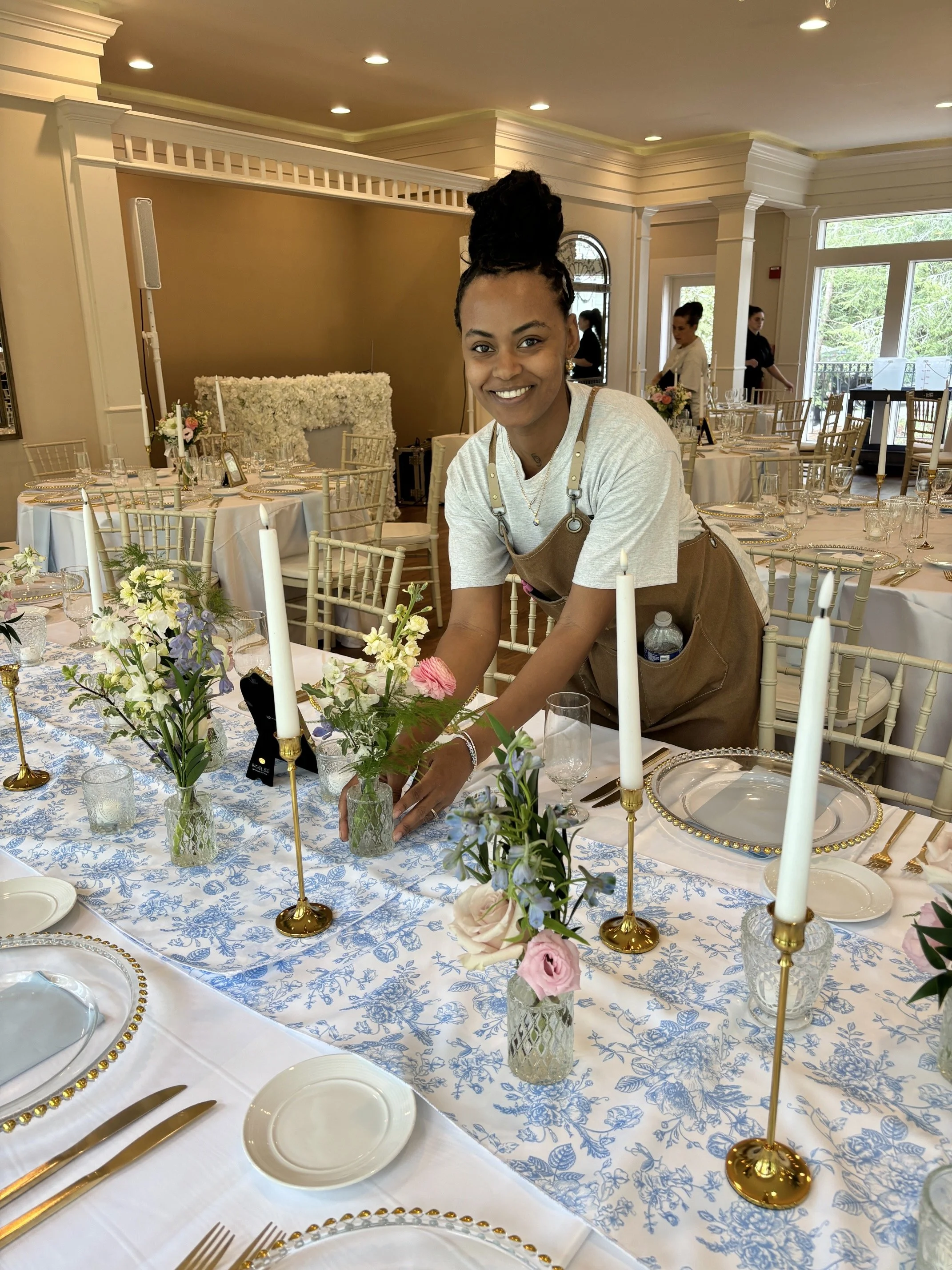 A woman arranging floral centerpieces on a beautifully decorated banquet table at an event venue with elegant table settings and floral arrangements.