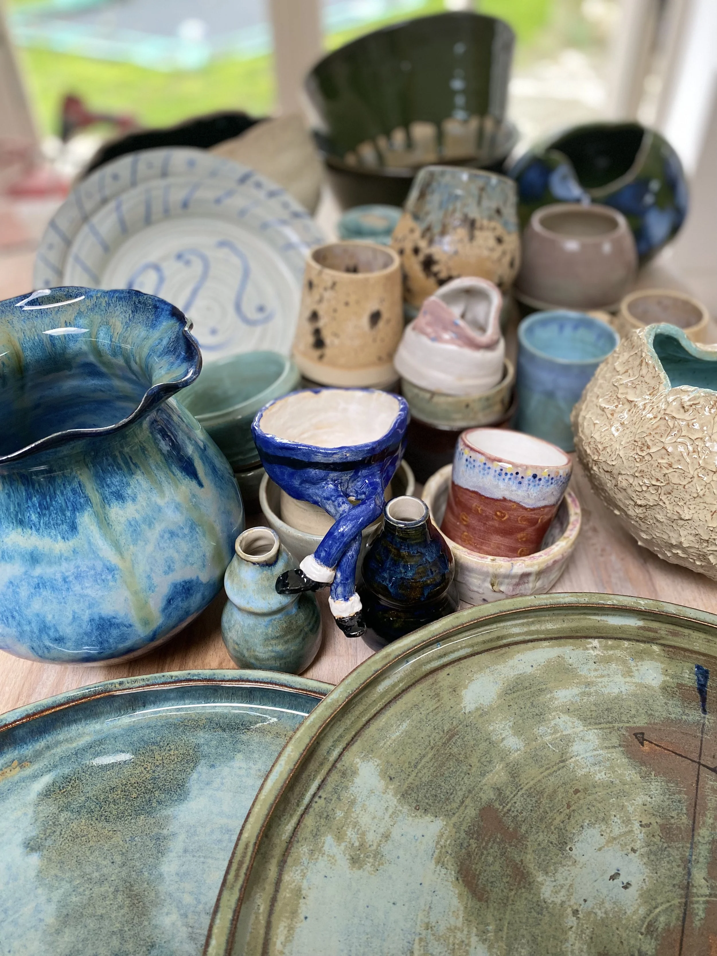 Collection of assorted handmade ceramic pottery and bowls of various shapes, sizes, and colors displayed on a wooden surface.