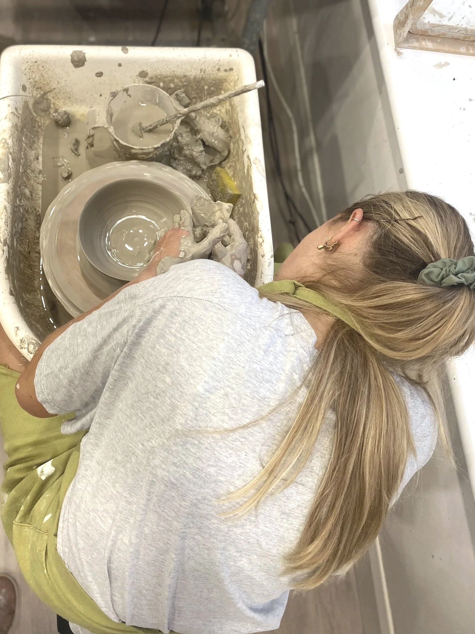 A person working in a pottery studio, shaping clay on a pottery wheel surrounded by water and clay splatters.