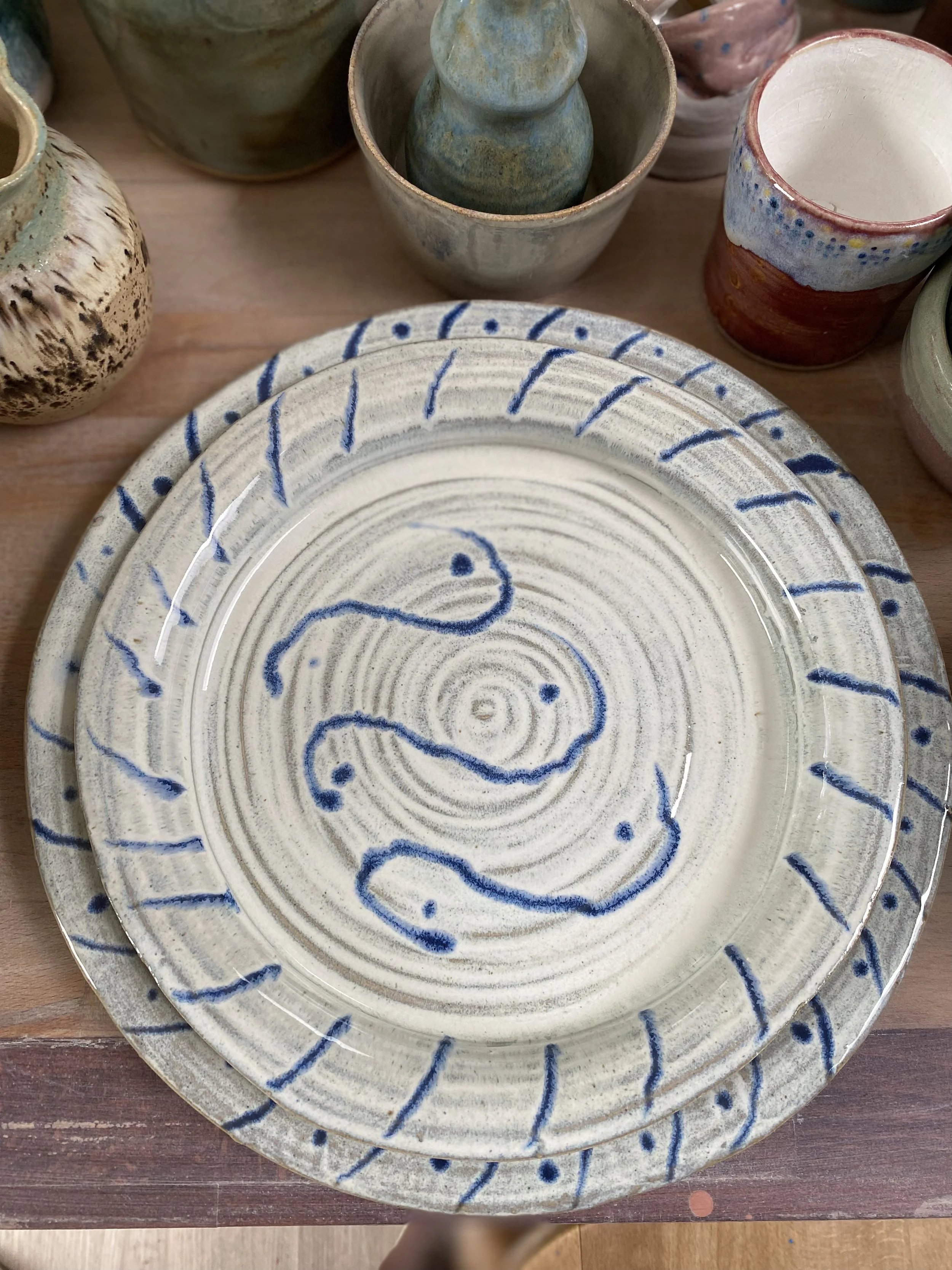 Ceramic plates with swirl and dot designs in blue, surrounded by various handmade cups and bowls.