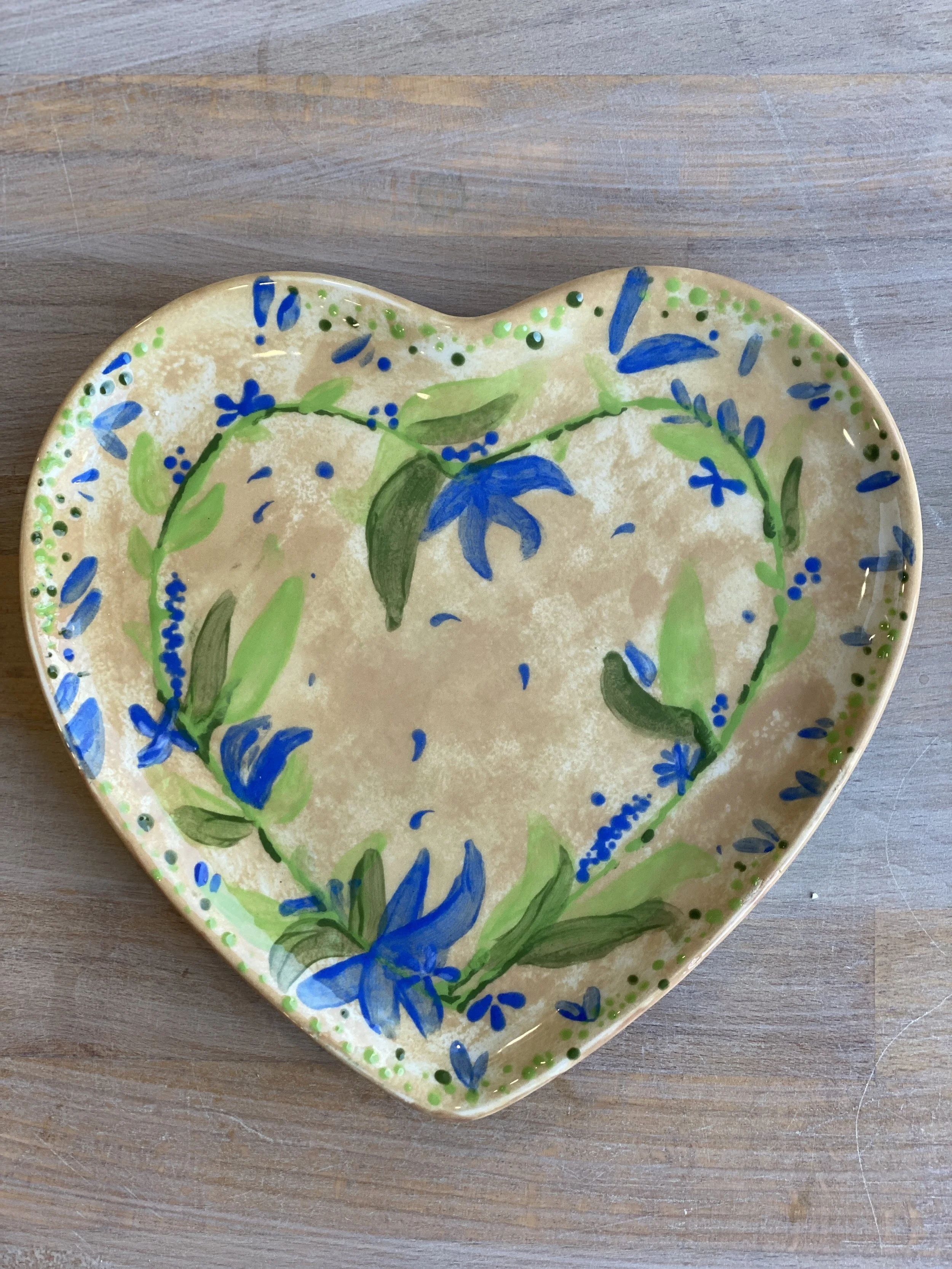 Heart-shaped decorative ceramic plate with hand-painted blue and green floral pattern on a wooden surface.