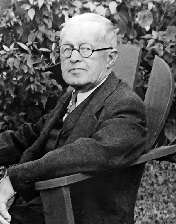 J.D. Shatford with glasses seated in a wooden chair outdoors
