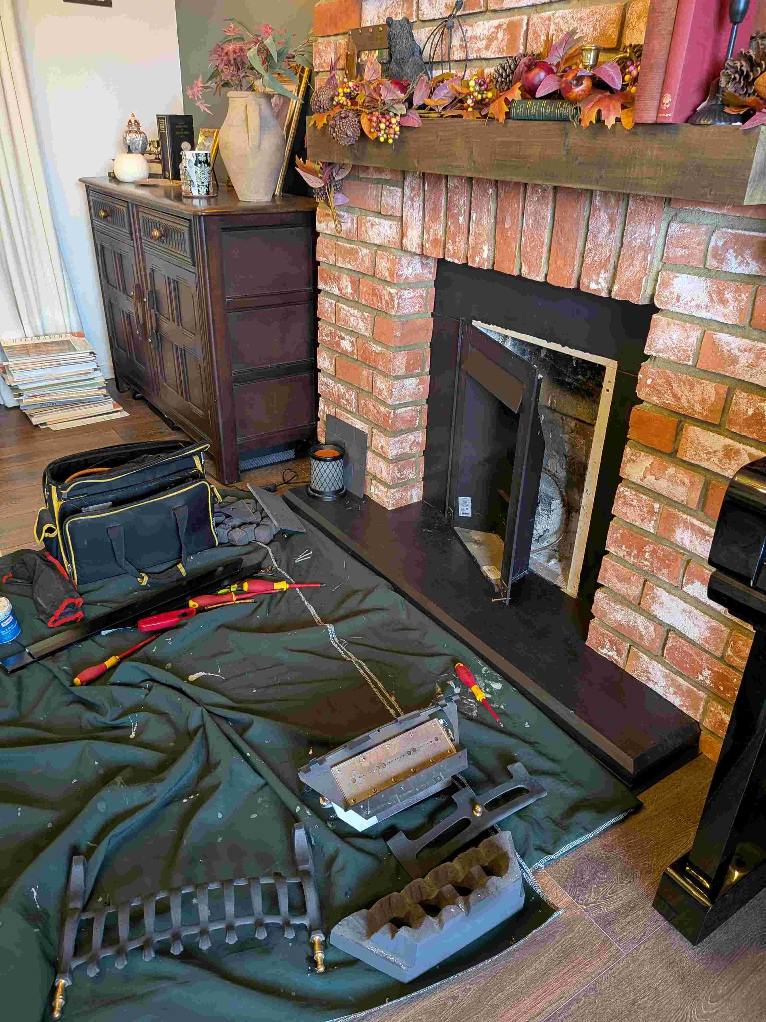 Tools and equipment laid out on a green drop cloth in front of a brick fireplace, with a toolbox, screwdrivers, and other technical tools visible.
