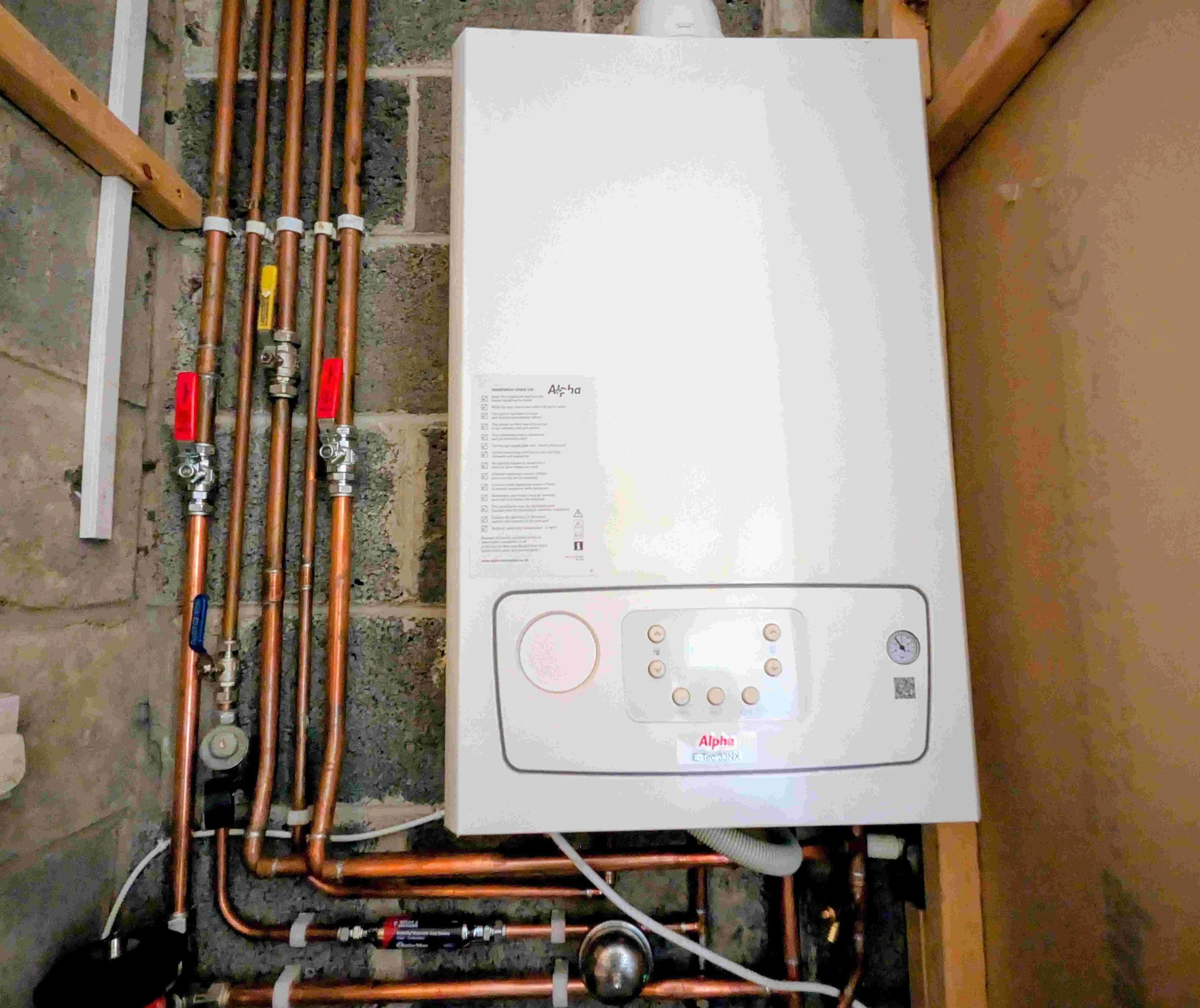 A white boiler unit installed on a wall with copper piping and valves connected to it.