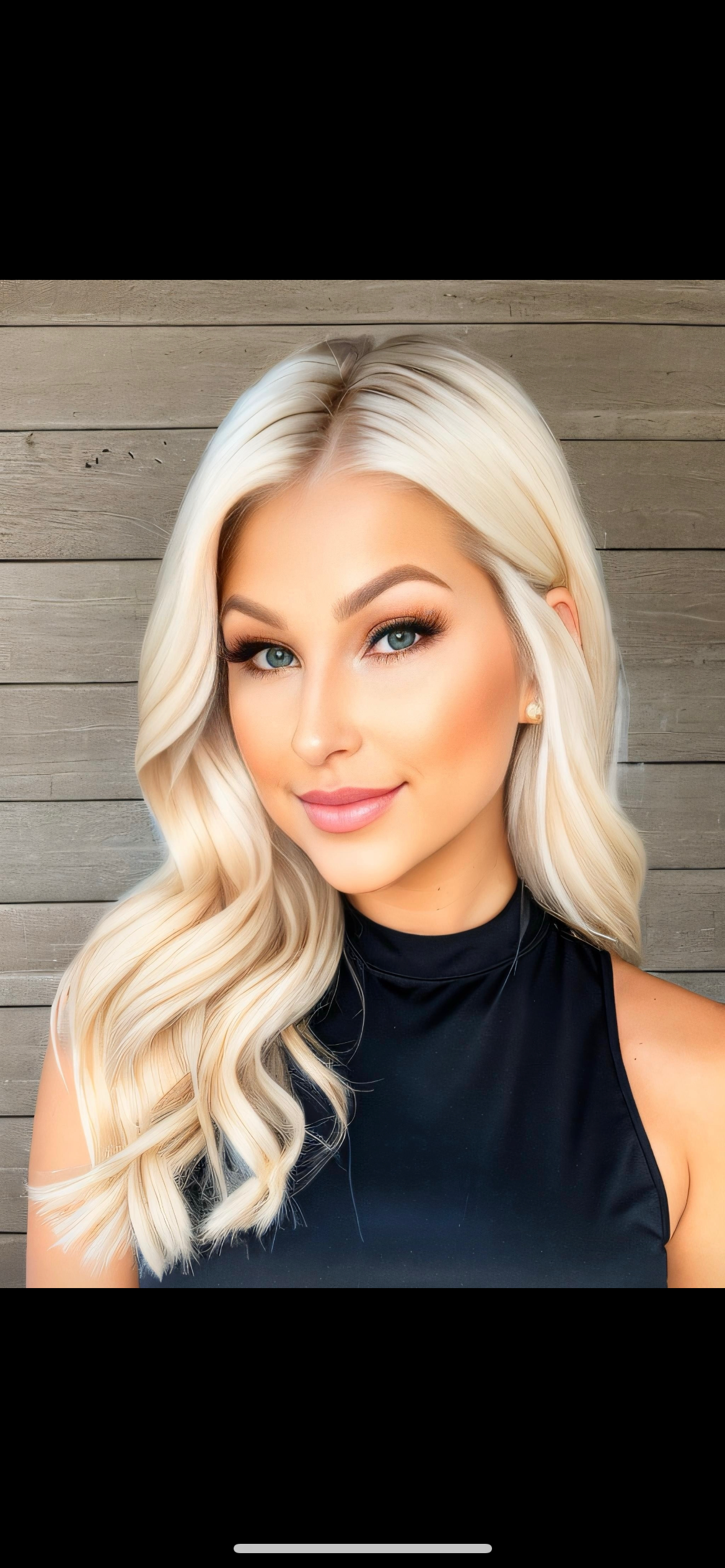Woman with long blonde hair, blue eyes, wearing a black top, against a wooden background.