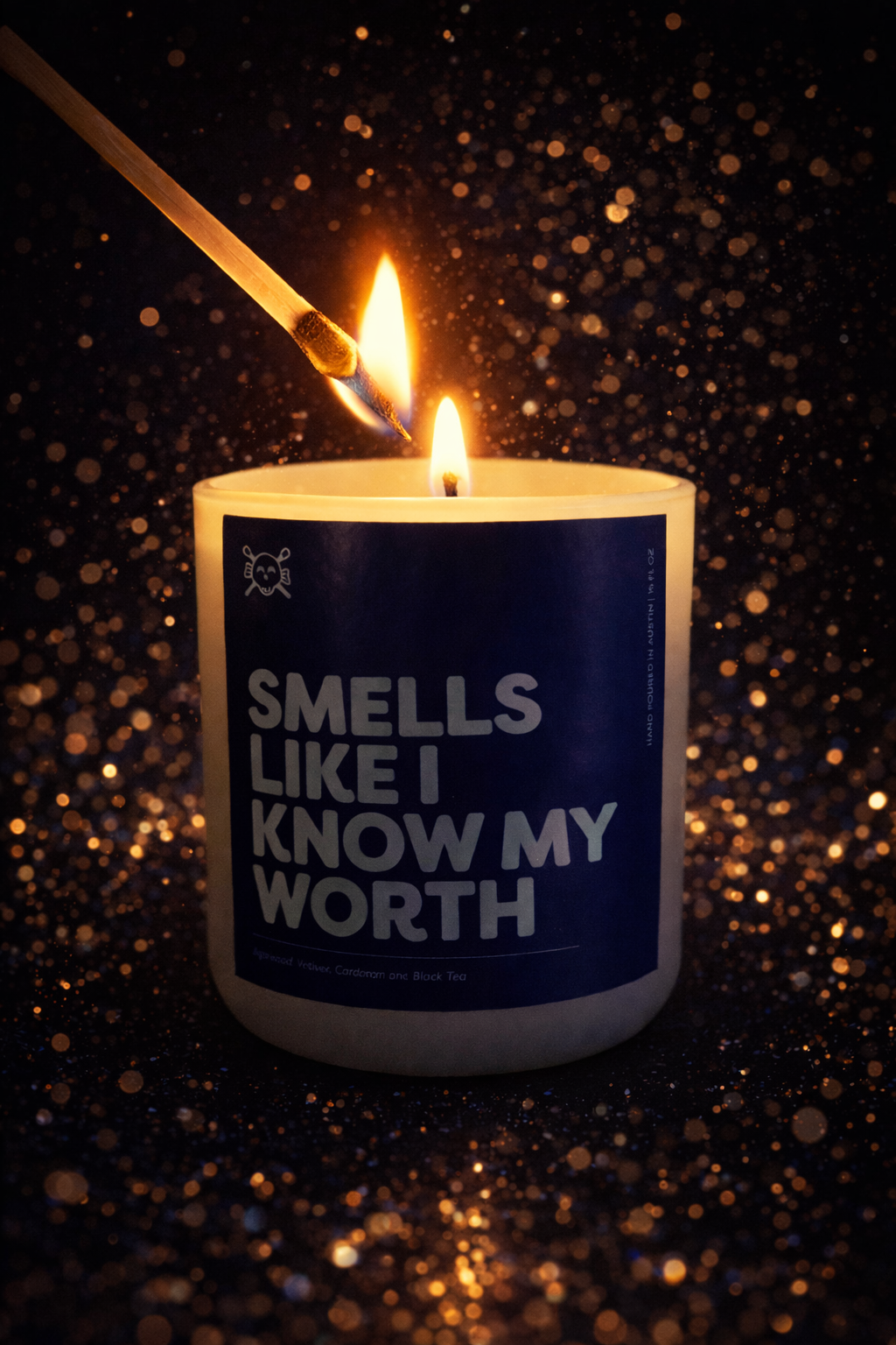 A lit candle with a matchstick being used to light it, against a dark background with golden bokeh effects. The candle has a label that reads 'Smells Like I Know My Worth'.