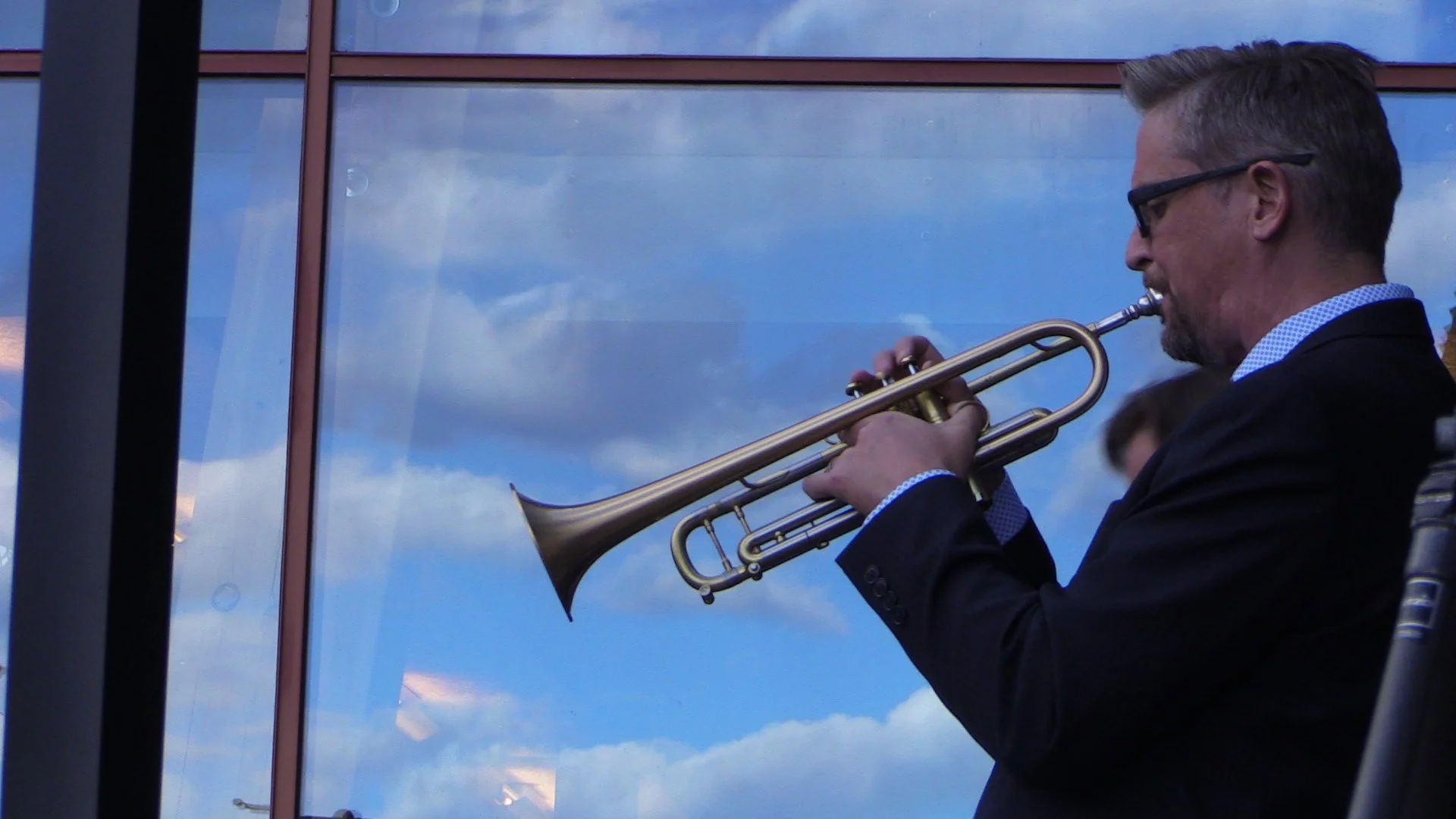 Man playing trumpet against a glass window background