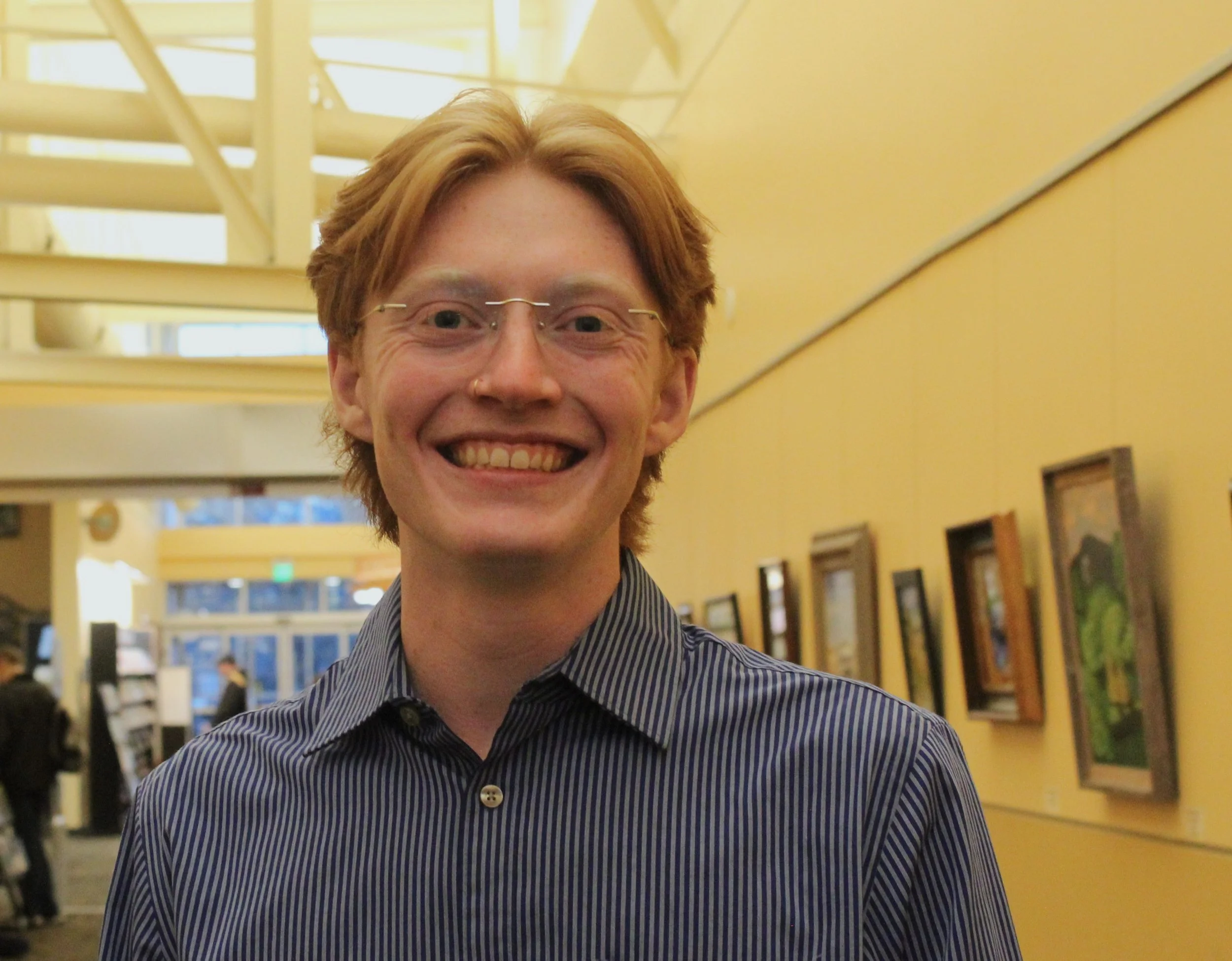 A person smiling in a gallery with artwork on the walls.