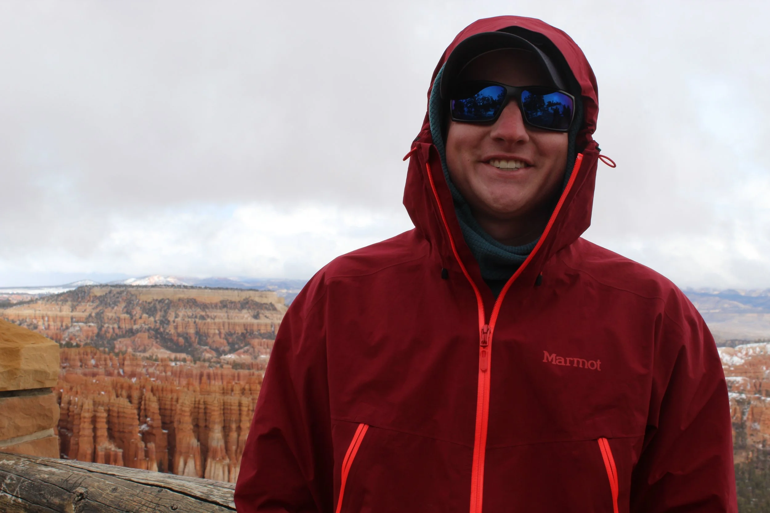 Person in red jacket and sunglasses standing in front of Bryce Canyon landscape.
