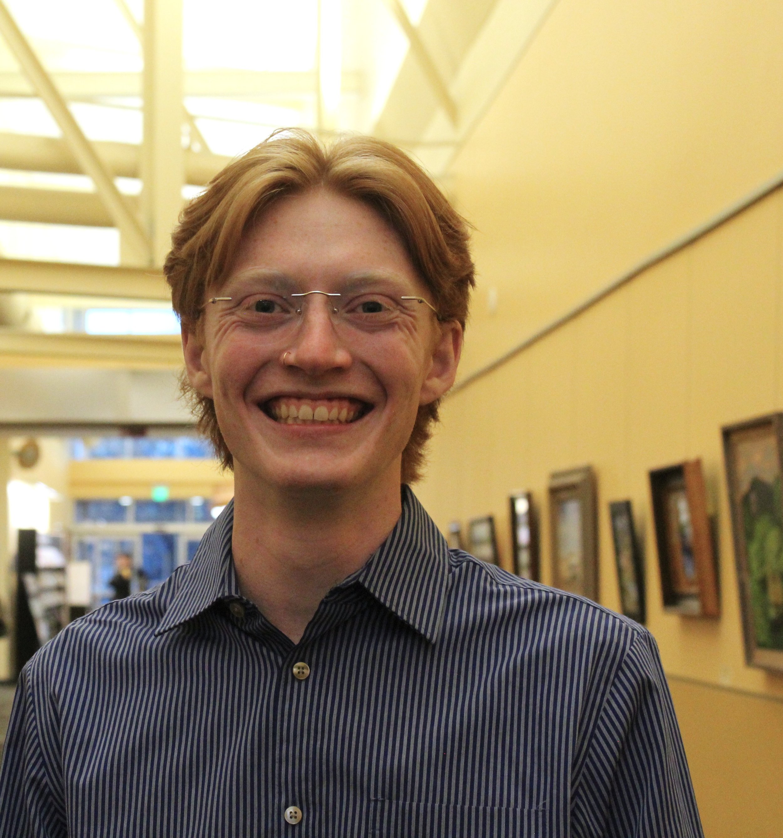 Smiling person wearing glasses and a striped shirt in an art gallery.