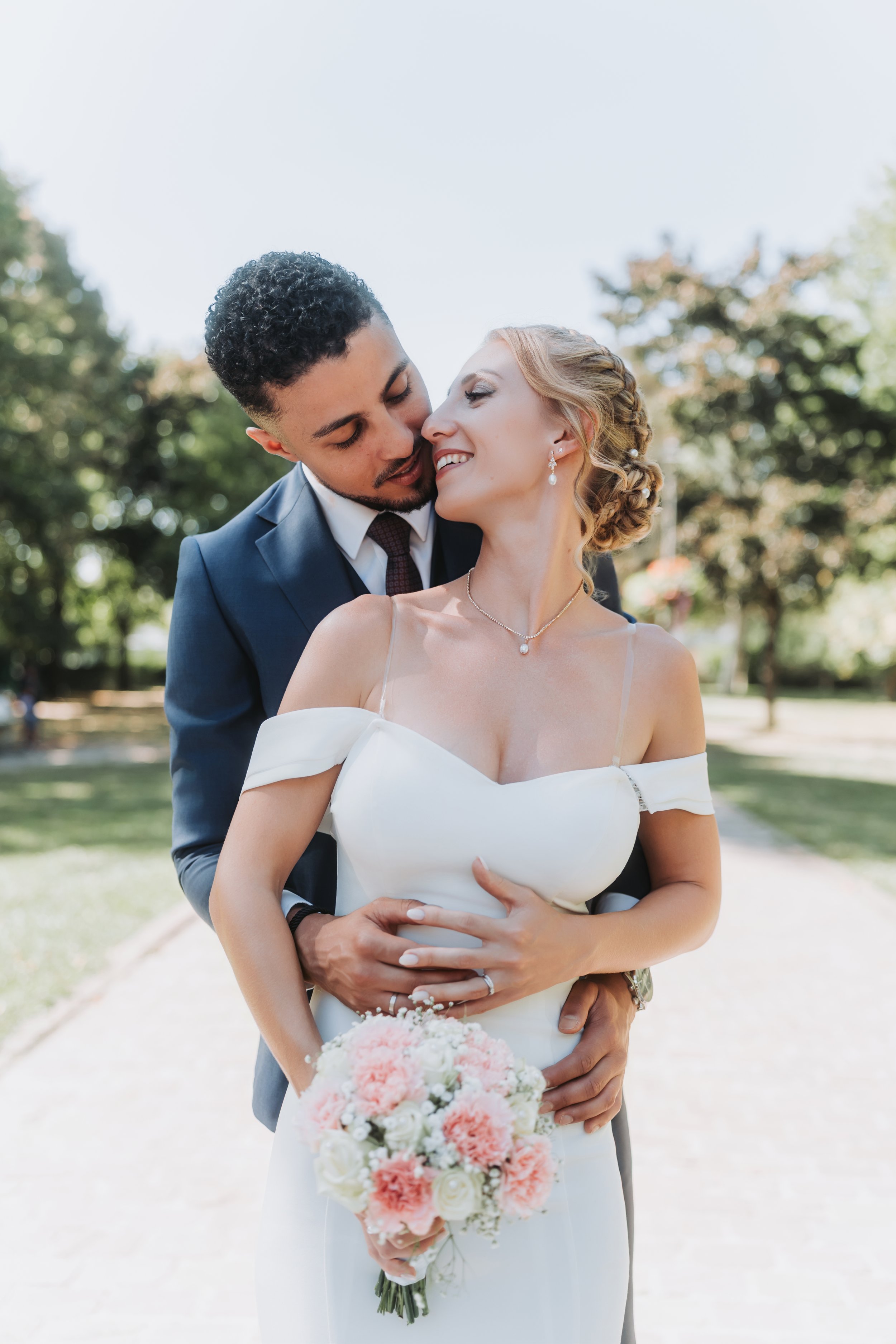 Un couple de mariés s'embrassant dans un parc, la femme tenant un bouquet de fleurs