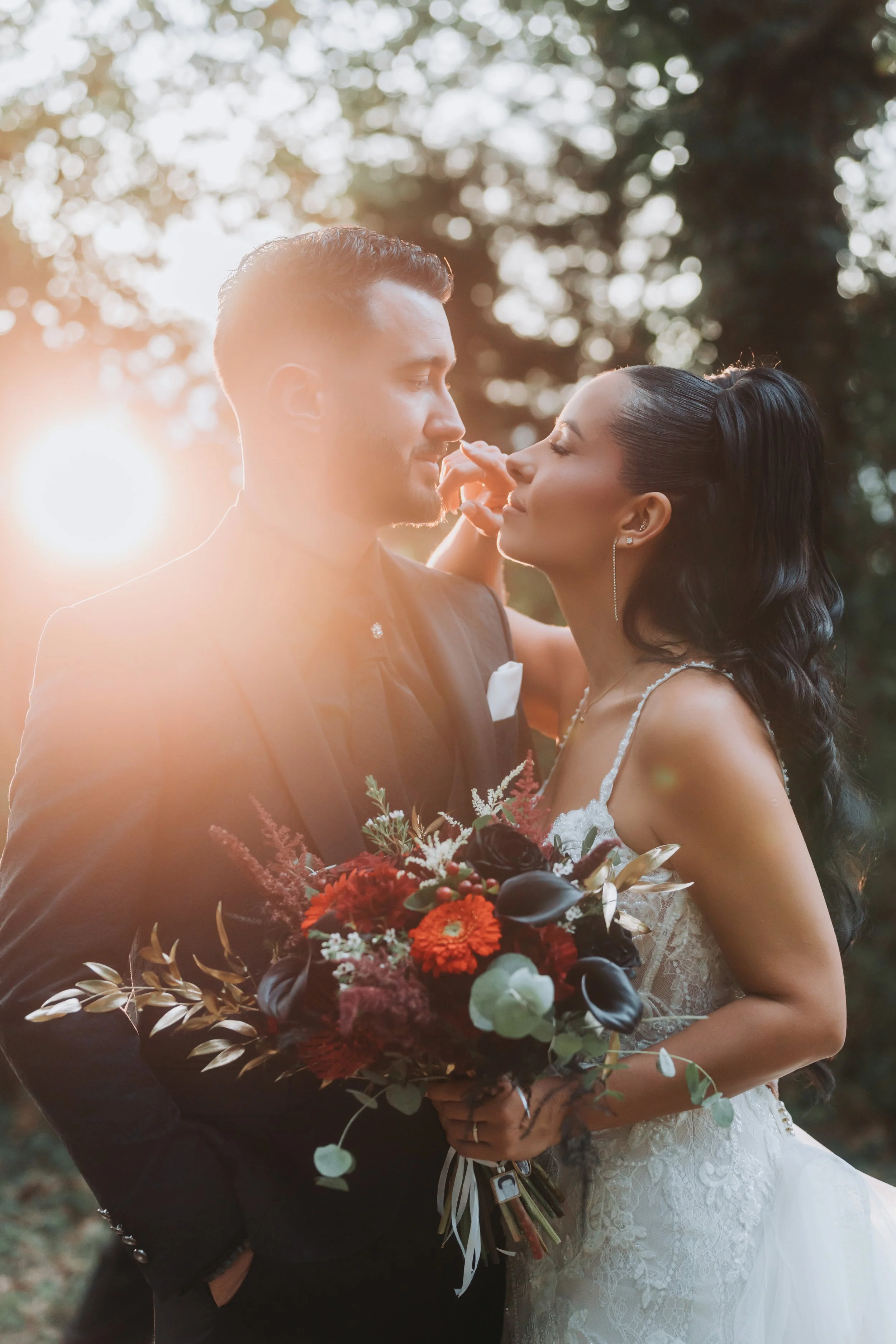 Un couple de mariés lors d'une séance photo en plein air au coucher du soleil, la femme tenant un bouquet de fleurs colorées.