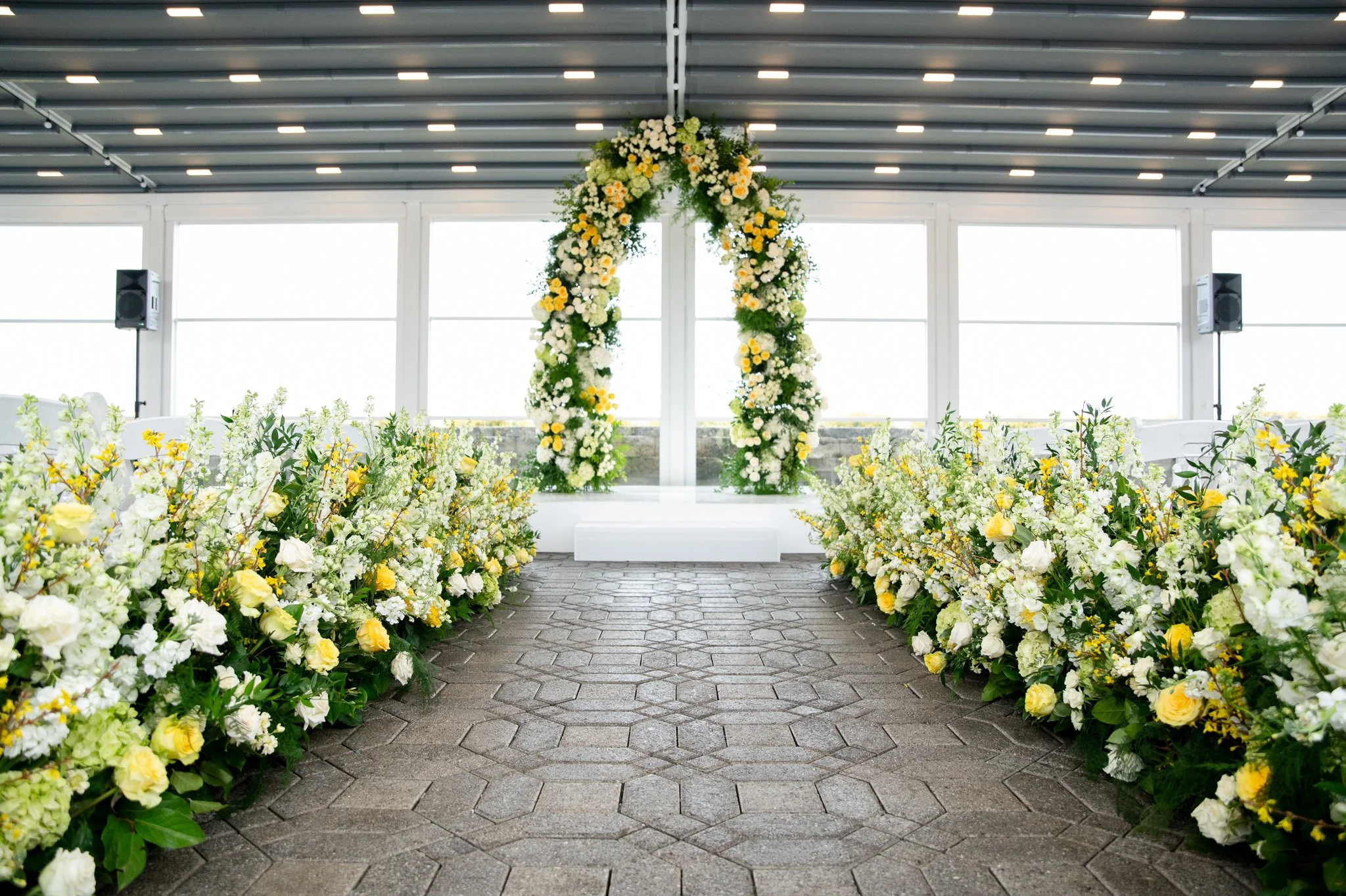 Stunning wedding ceremony setup featuring a lush yellow and white floral aisle leading to a grand floral arch. Luxury floristry and event design by Glitzed Events at Marina Del Rey in Bronx, NY