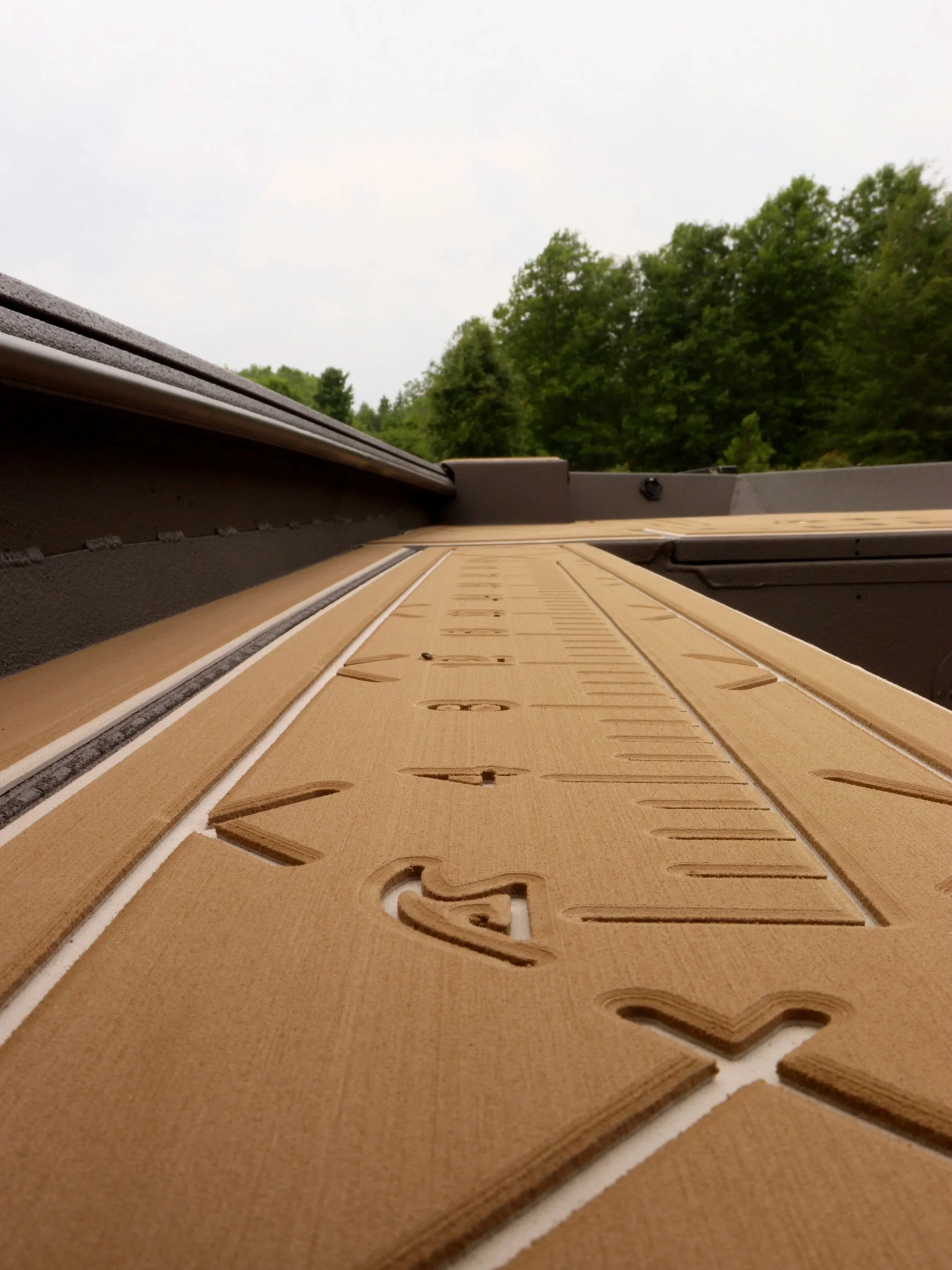 Close-up photo of a wooden outdoor calendar with carved numbers and lines, mounted on a surface with greenery and trees in the background.