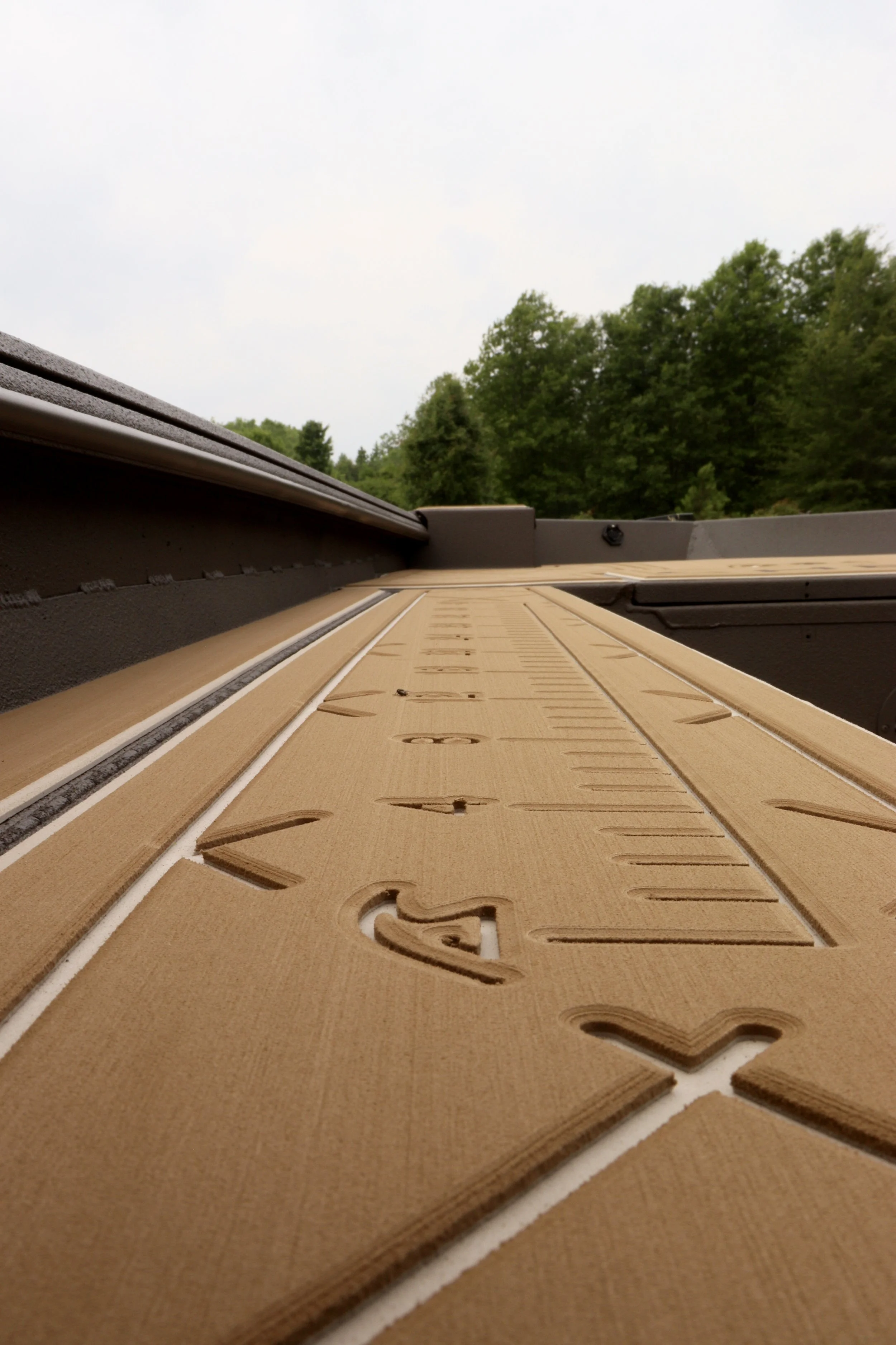 View from inside a boat with camouflage pattern, showing the bow, with a GMC Sierra truck and pet carriers in the background on a gravel area near some green trees and shrubs during daylight.