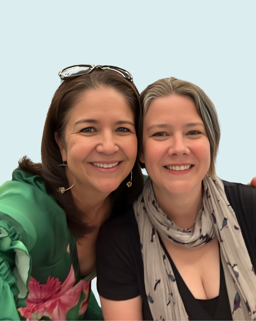 Two women smiling for a close-up photo against a light blue background.