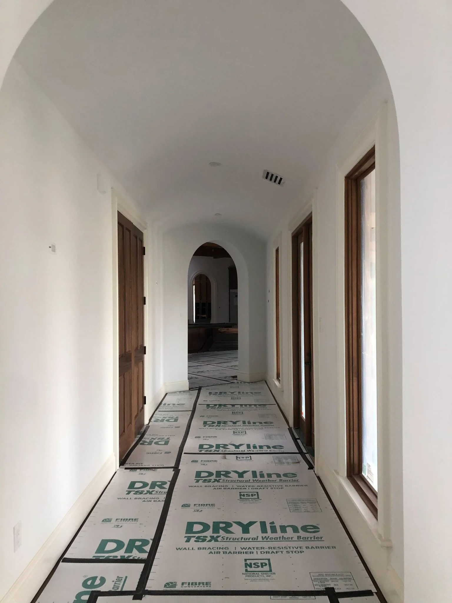 Empty hallway with white walls, wooden doors, and windows, with construction materials on the floor.