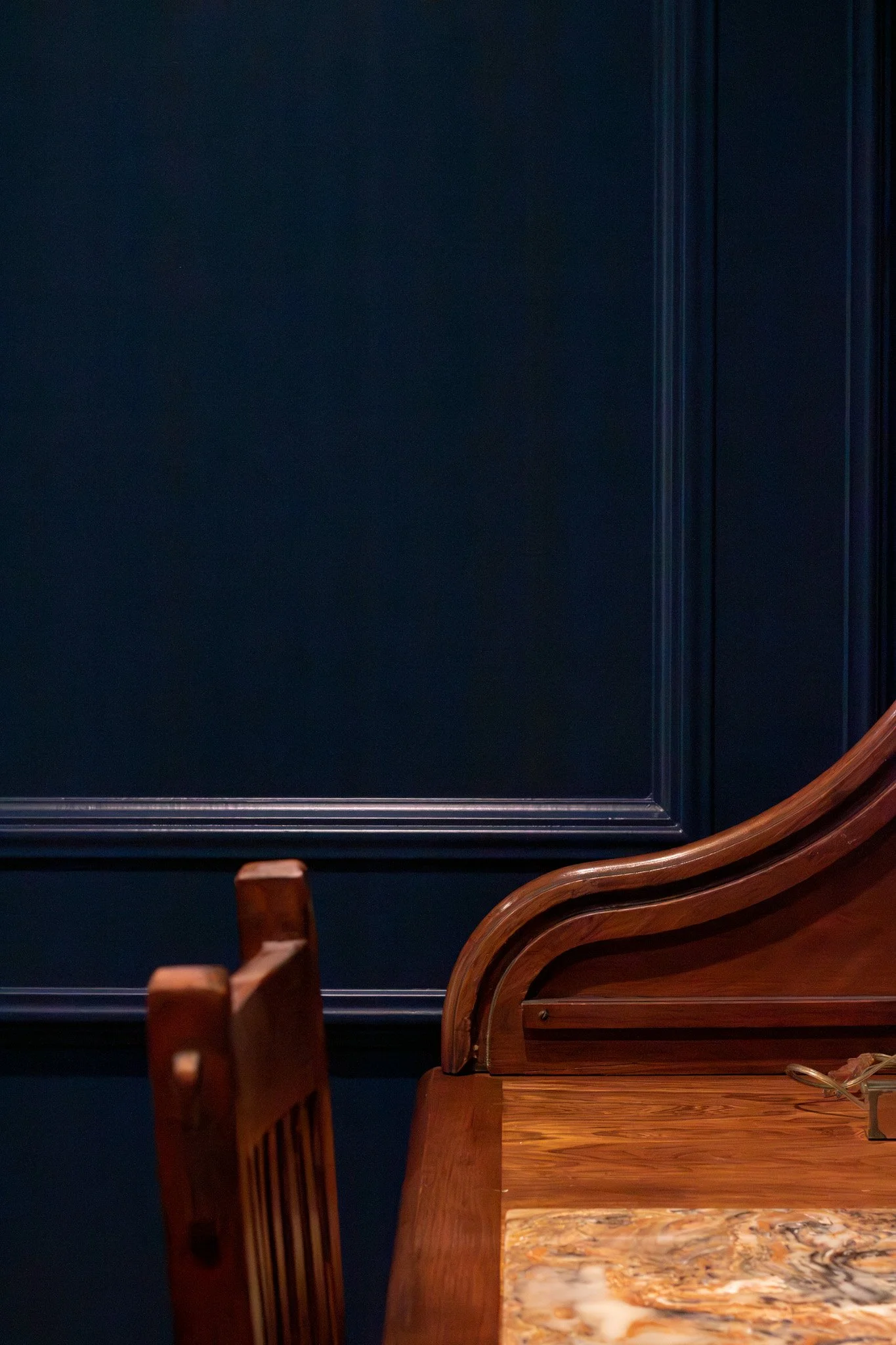 Part of a wooden desk and chair against dark blue wall paneling.