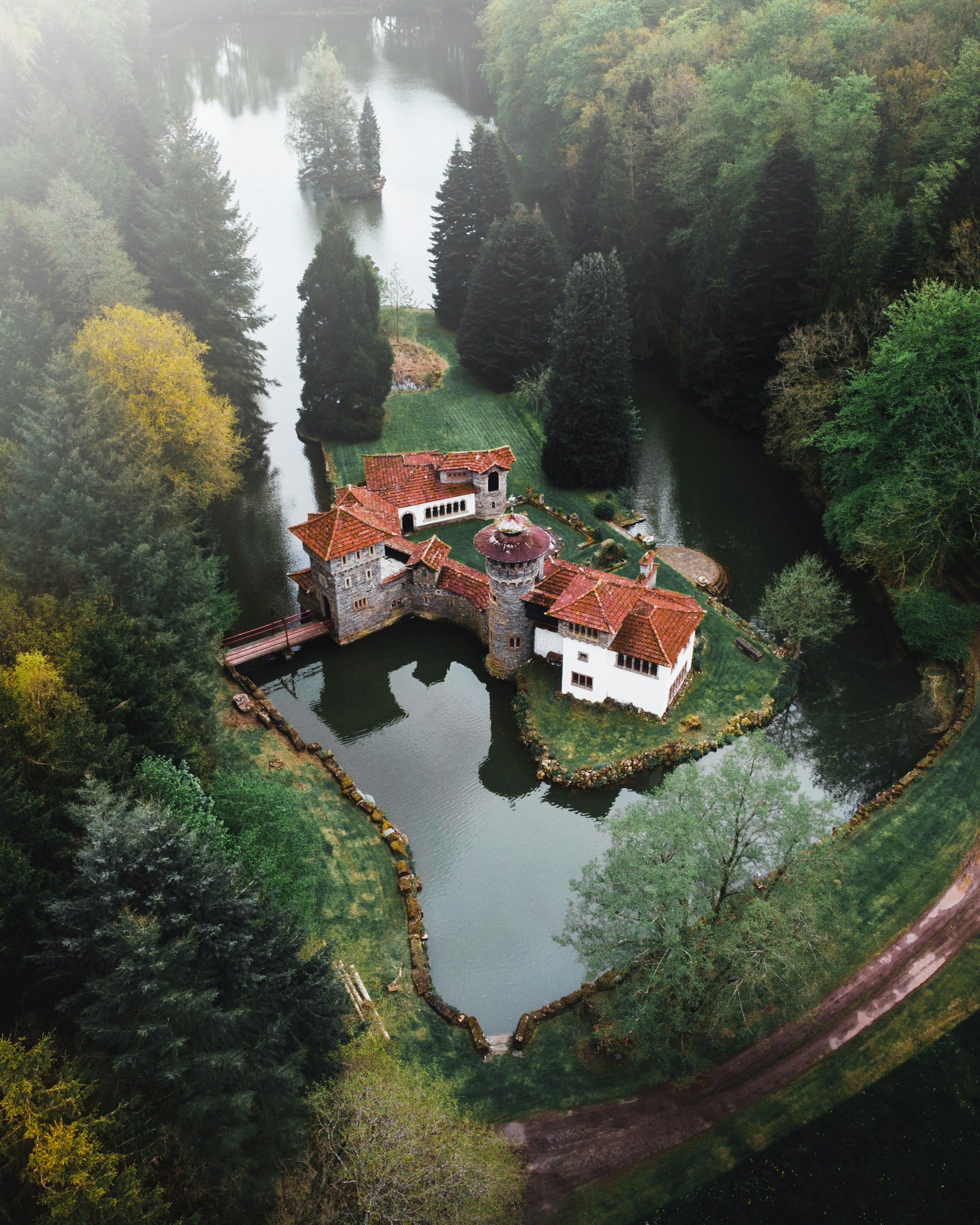 large estate on an island surrounded by a moat looking river with a bridge leading to an old brick building with a large grass yard
