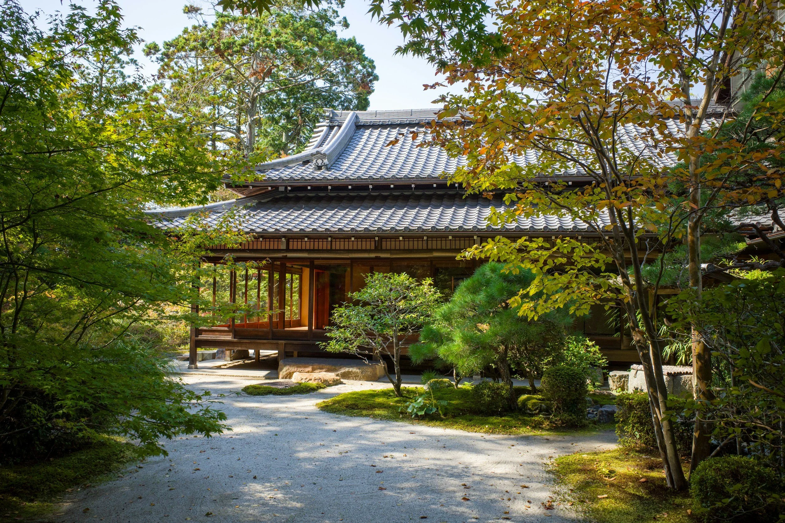 a japanese styled house with a garden made up of a gravel pathway and plants and trees and moss