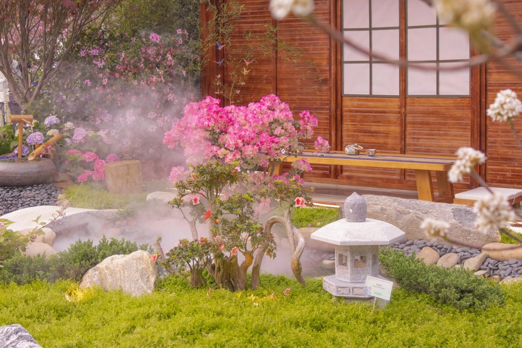 an onsen pool in a yard with plants and flowers and a japanese stone lantern statue