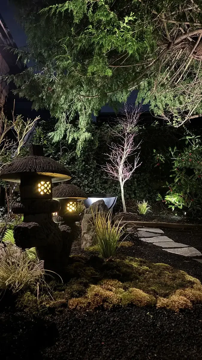 Illuminated stone lanterns, moss and stepping stones in a landscaped garden.