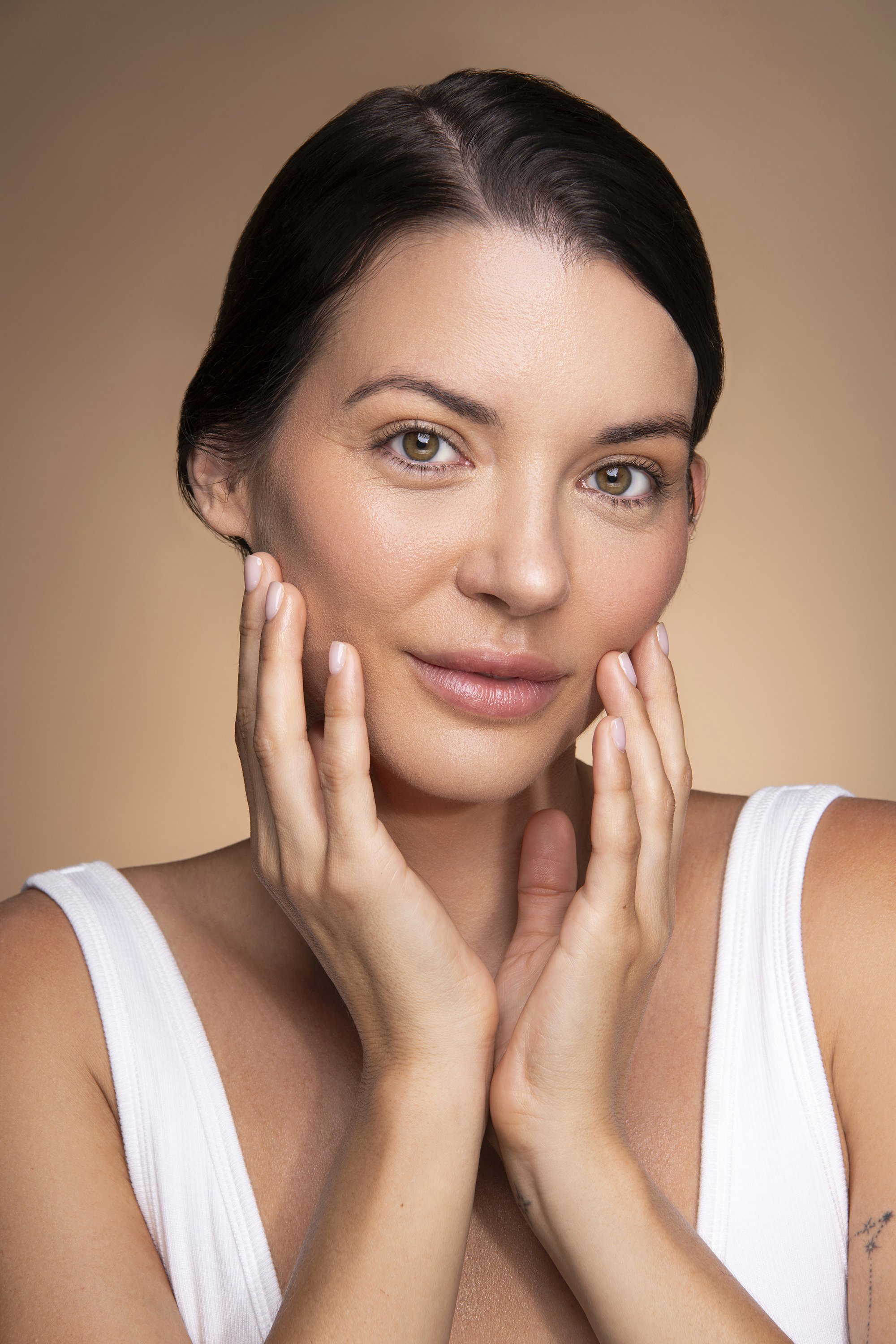 Atlanta skincare advertising photography featuring a female model with natural skin texture and polished beauty makeup for AYA Skin, photographed by commercial beauty photographer Caitlin Tabilog against a minimal beige seamless backdrop. 