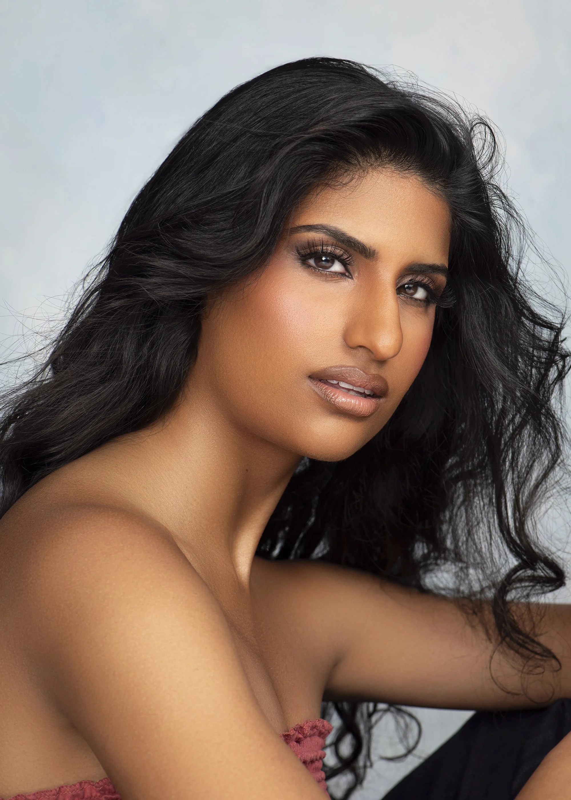 Luxury beauty portrait photographed with soft studio lighting at Industry Makeup Academy in Atlanta, Georgia. Professional model from Forward The Agency posing against a hand-painted blue backdrop with polished makeup and elegant styling. Beauty and 