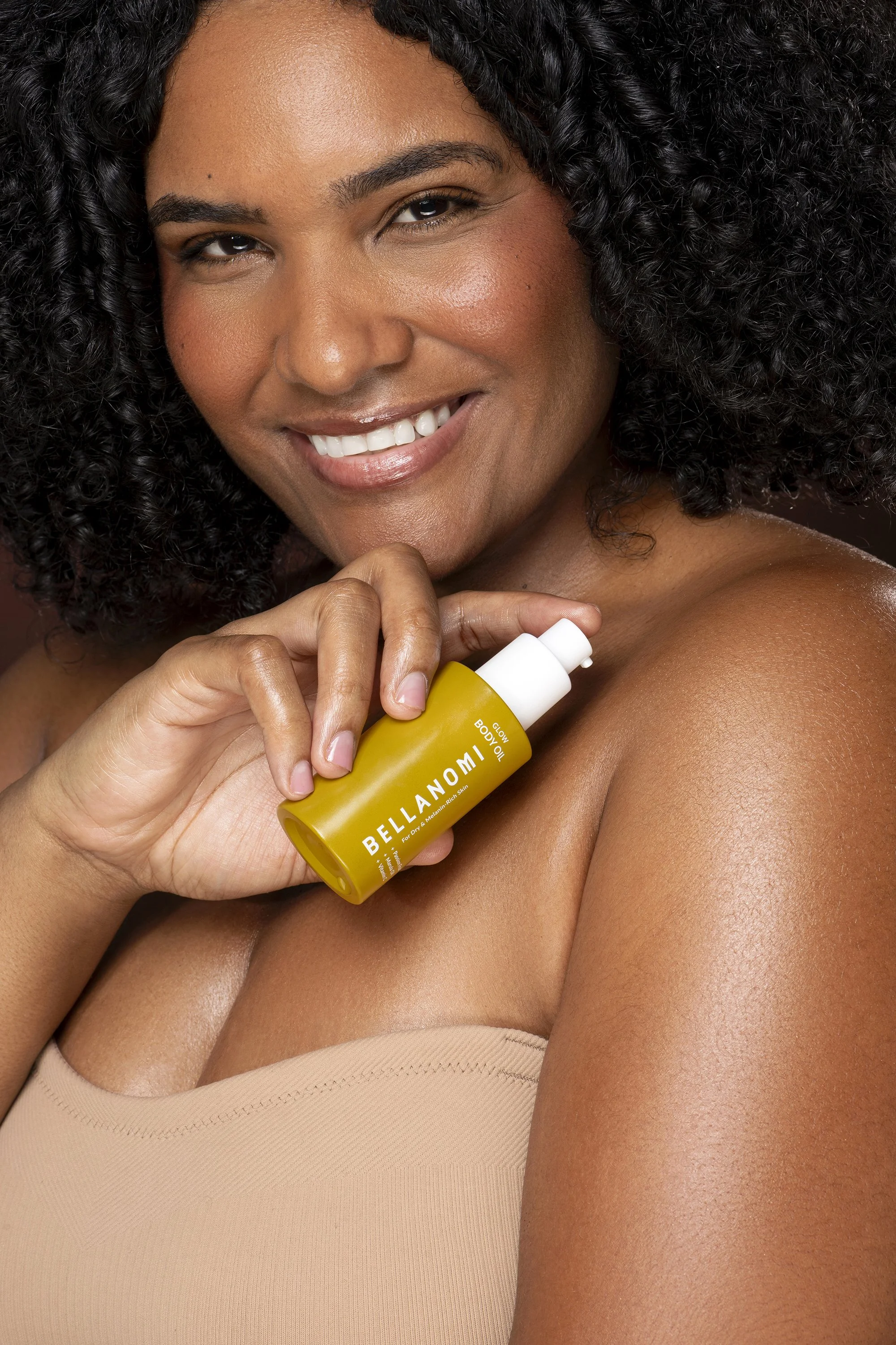 Bellanomi Skincare beauty campaign featuring Bianca Nolden, a model signed with Forward The Agency, smiling while holding a yellow skincare bottle in a natural light studio loft in Milton, Georgia. Luxury beauty advertising photography by Atlanta pho