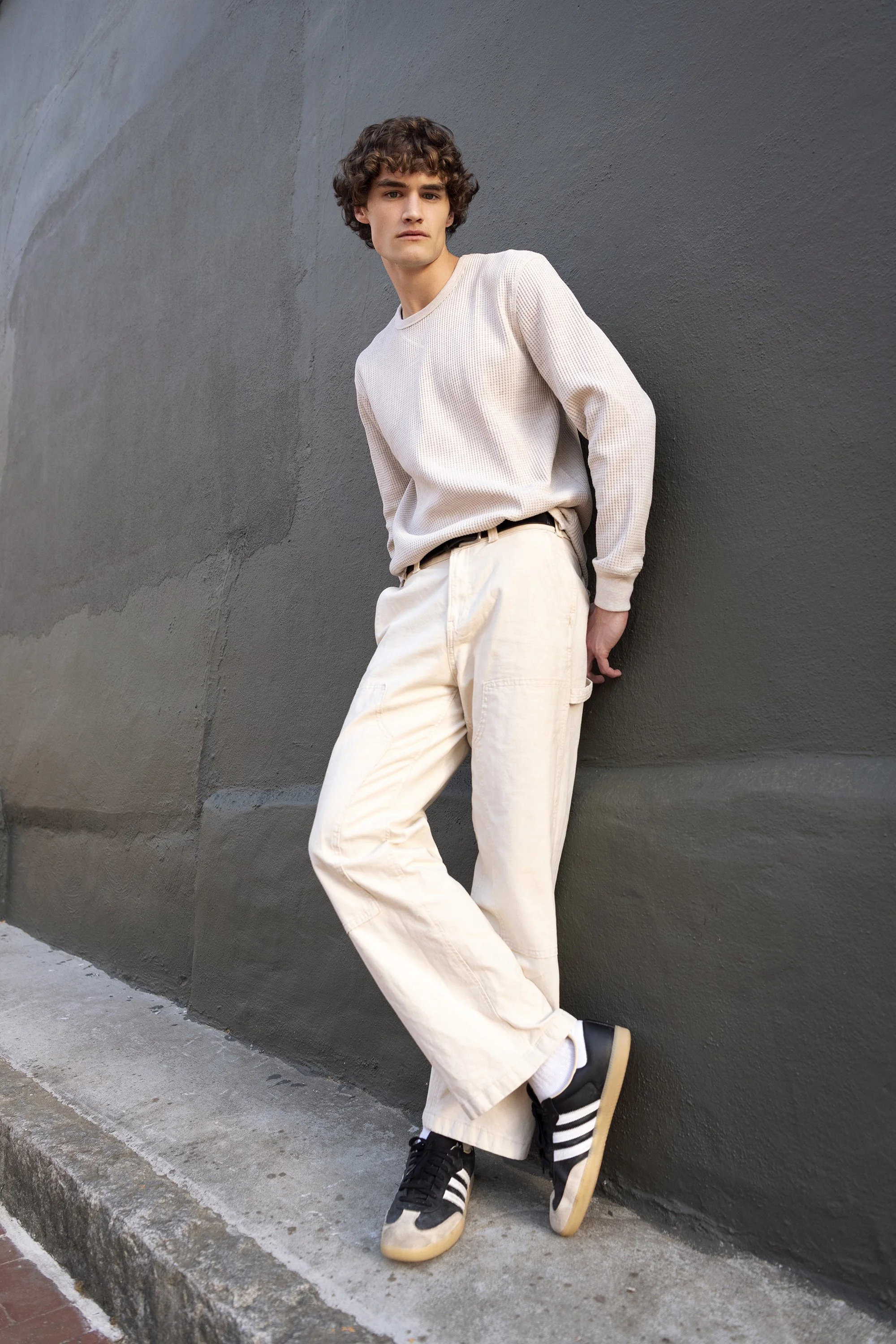 Fashion portrait of Sam Mauldin, a model represented by Forward The Agency, wearing a black T-shirt and dark jeans while posing outdoors against a beige background. Menswear and fashion photography by Atlanta portrait photographer Caitlin Tabilog.