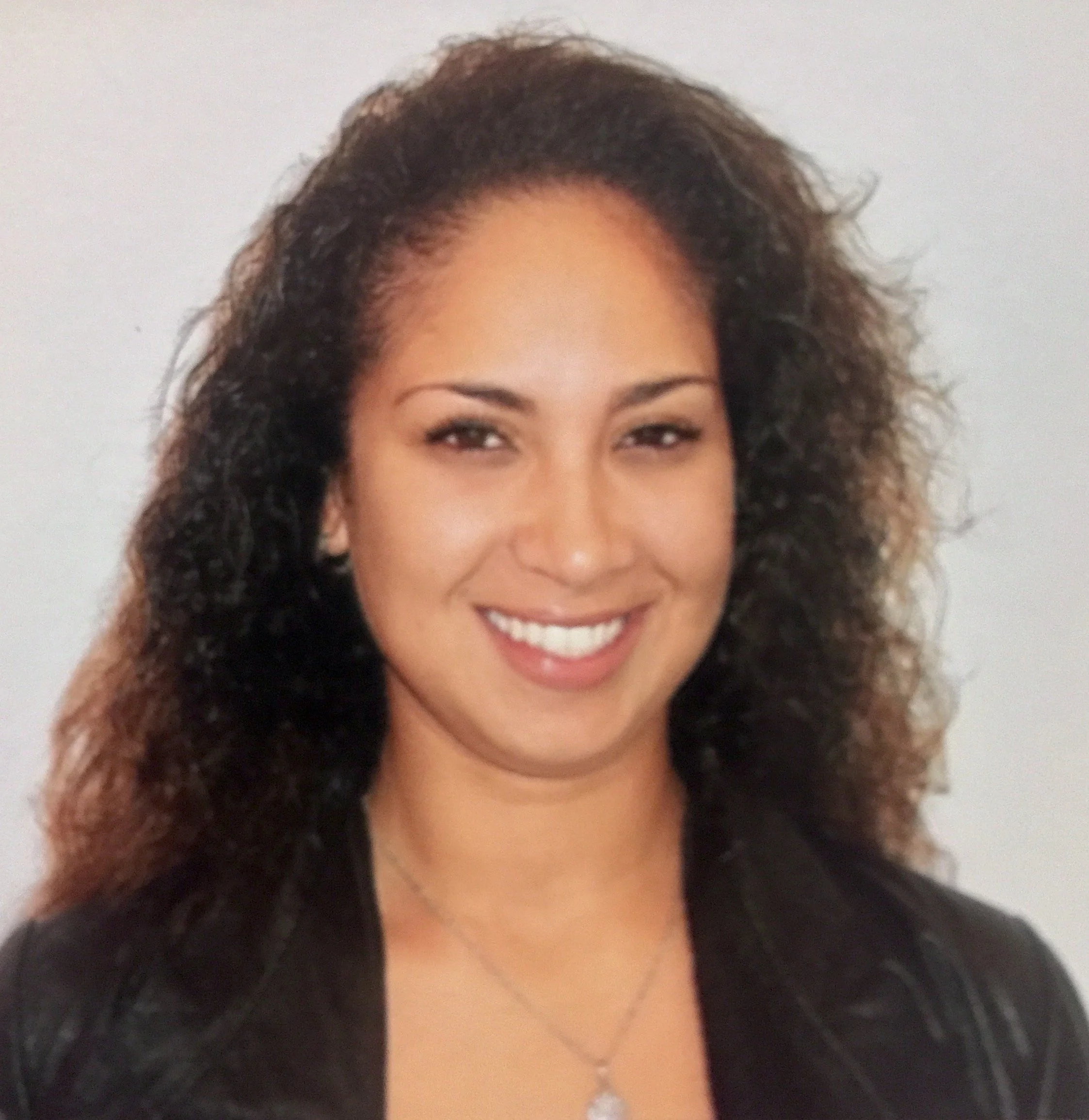 A woman with wavy brown hair and brown skin smiling with a neutral background